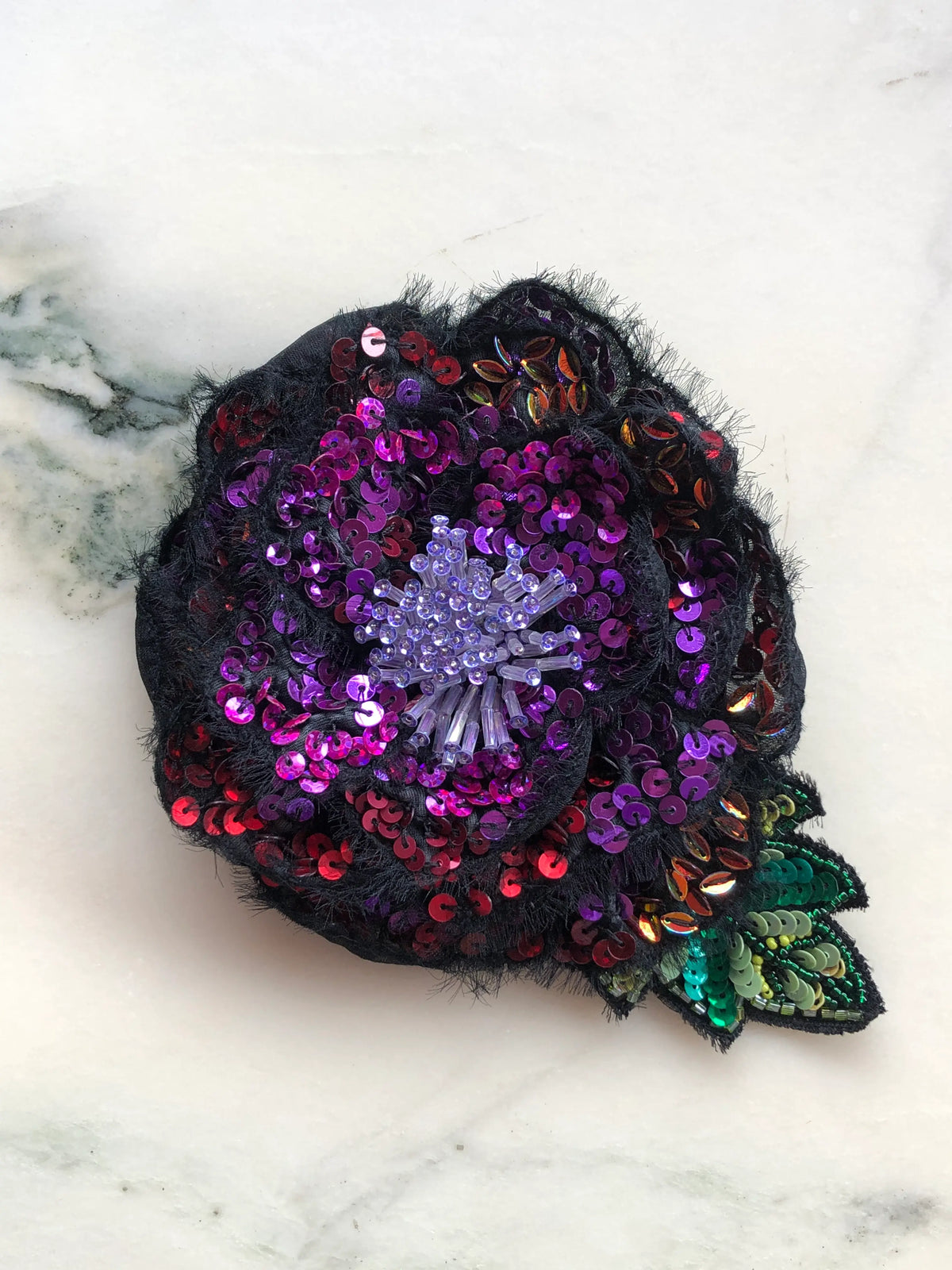 Broochella Men's Luminosa Small Flower Brooch Pin in blue, featuring layered black fabric petals embellished with shimmering navy, sapphire blue and iridescent sequins, a delicate ivory beaded centre and decorative sequinned leaves. A statement floral brooch for men's blazers, jackets and occasionwear.