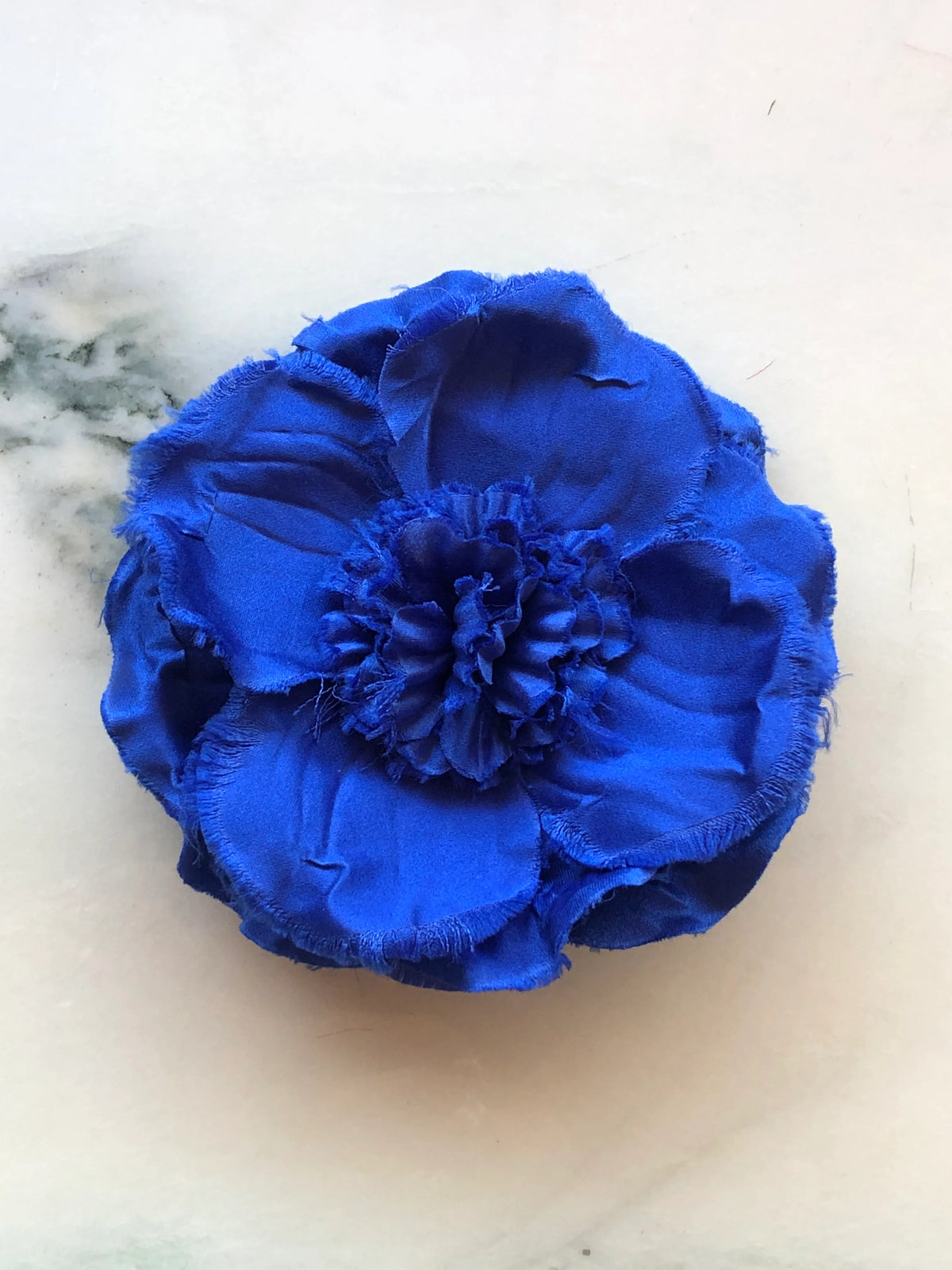 Broochella Men’s Malva Flower Brooch in vibrant cobalt blue, a handmade designer fabric flower with layered raw-edge petals and a textured ruffled centre, photographed on white marble.