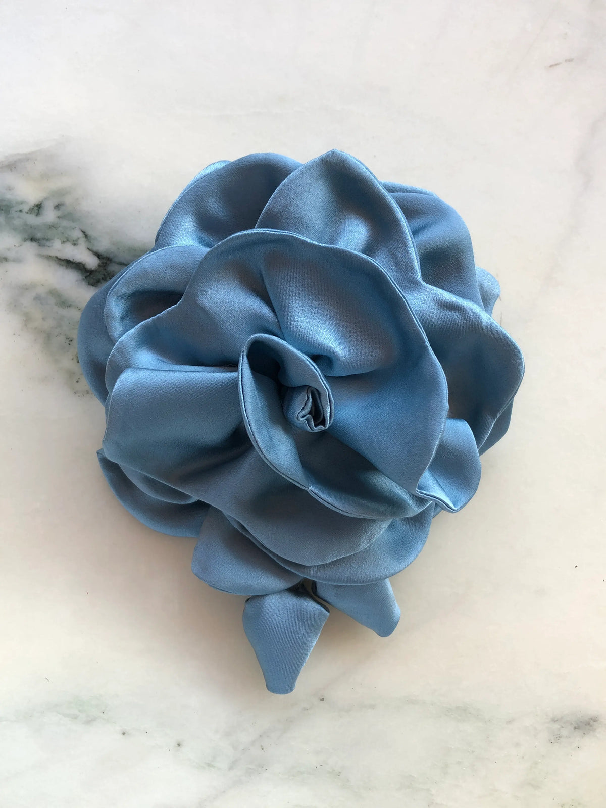 Broochella handmade designer satin Rosetta flower brooch in blue with sculptural layered petals and trailing flower buds, photographed on white marble.