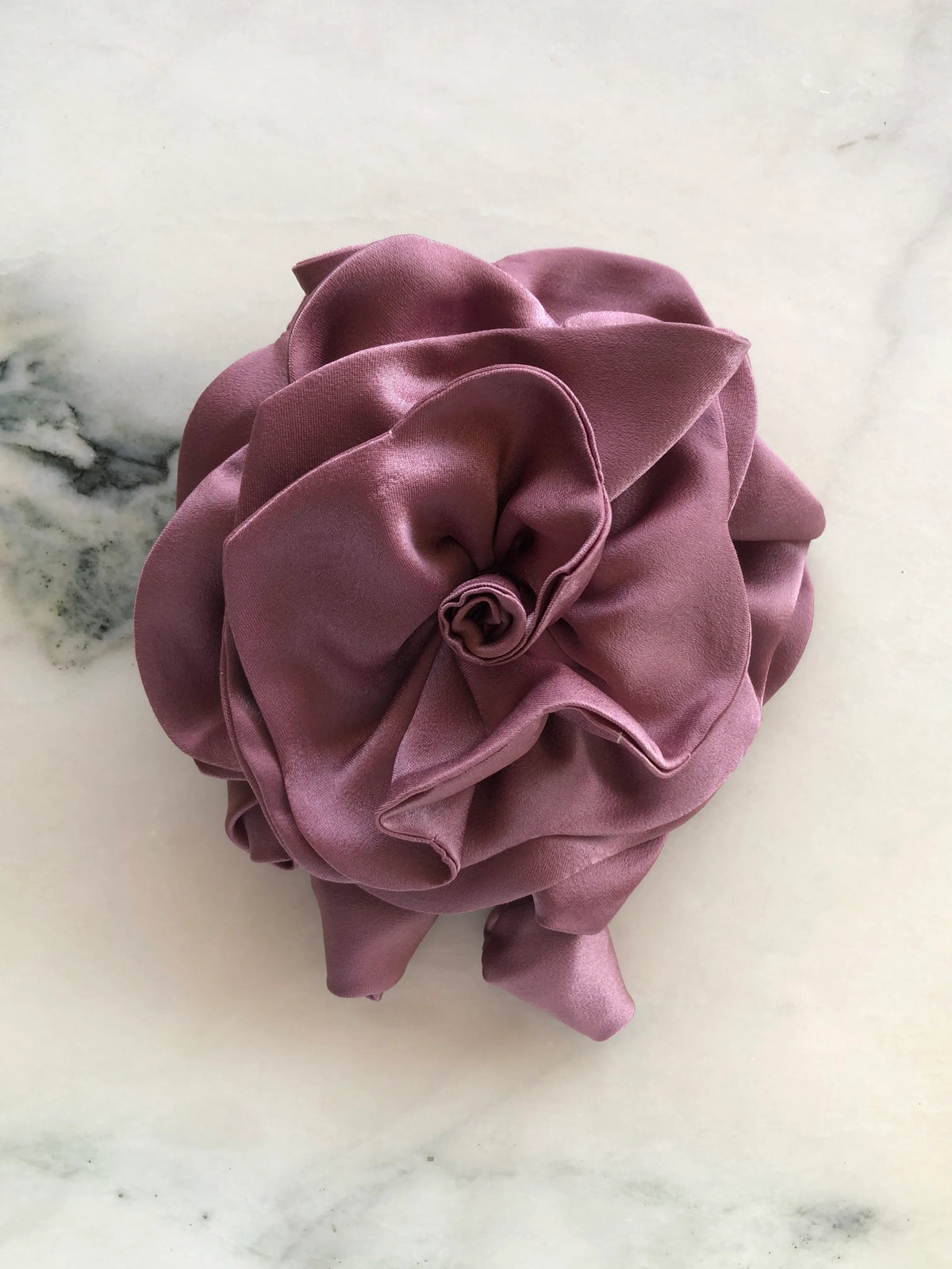 Broochella handmade designer satin Rosetta flower brooch in blush pink with sculptural layered petals and trailing flower buds, photographed on white marble.