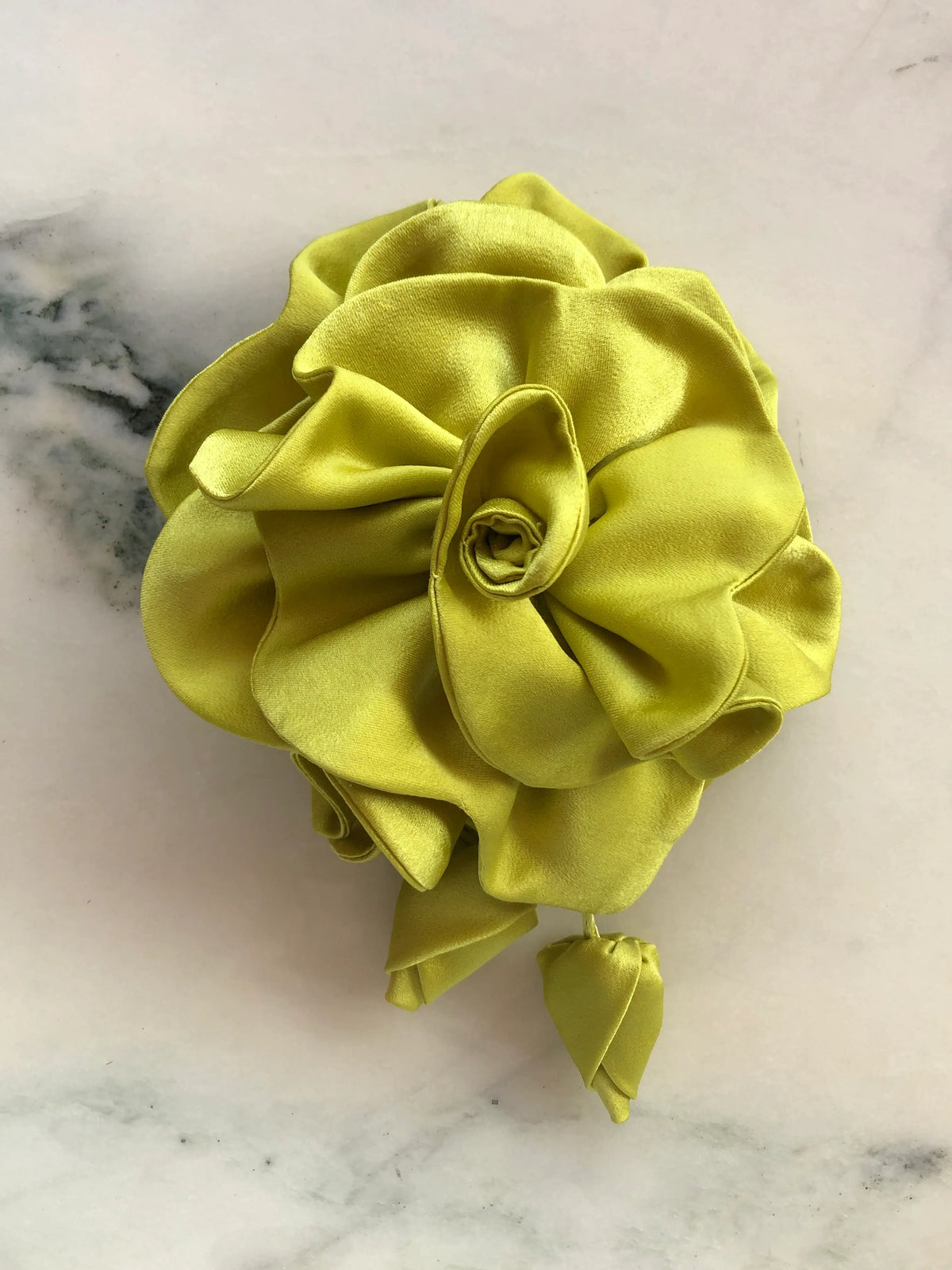 Broochella handmade designer satin Rosetta flower brooch in chartreuse with sculptural layered petals and trailing flower buds, photographed on white marble.
