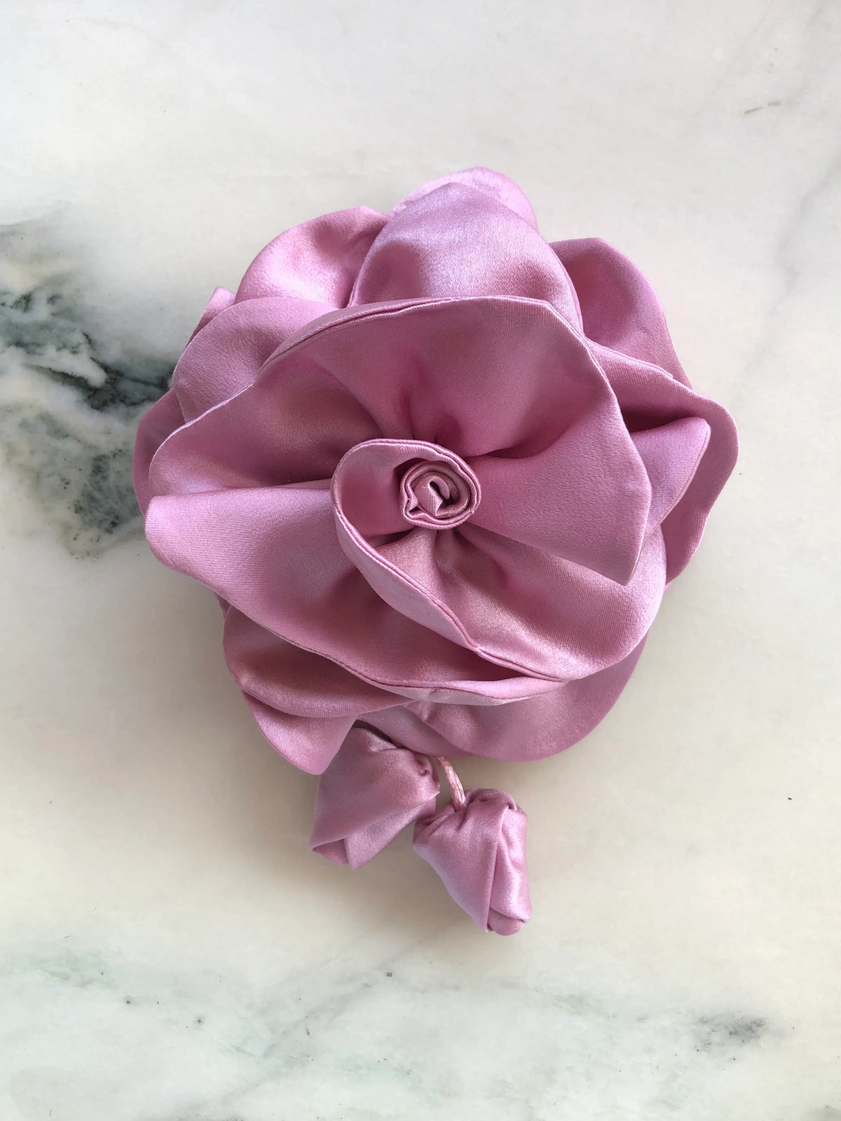 Broochella handmade designer satin Rosetta flower brooch in pink with sculptural layered petals and trailing flower buds, photographed on white marble.