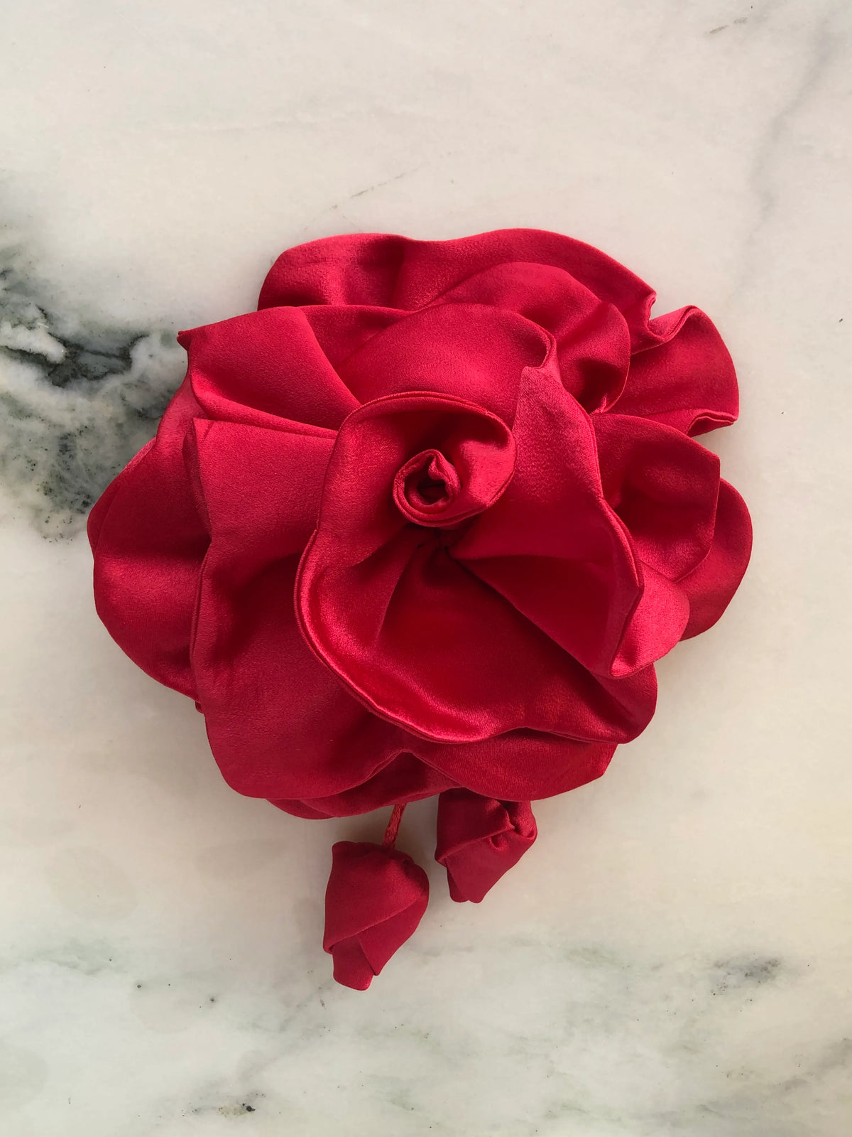 Broochella handmade designer satin Rosetta flower brooch in red with sculptural layered petals and trailing flower buds, photographed on white marble.