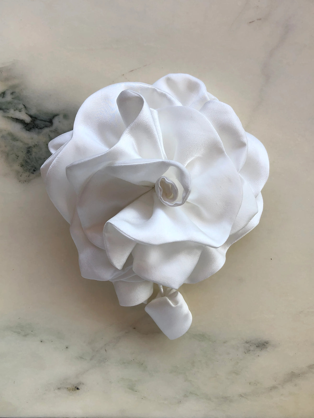 Broochella handmade designer satin Rosetta flower brooch in white with sculptural layered petals and trailing flower buds, photographed on white marble.