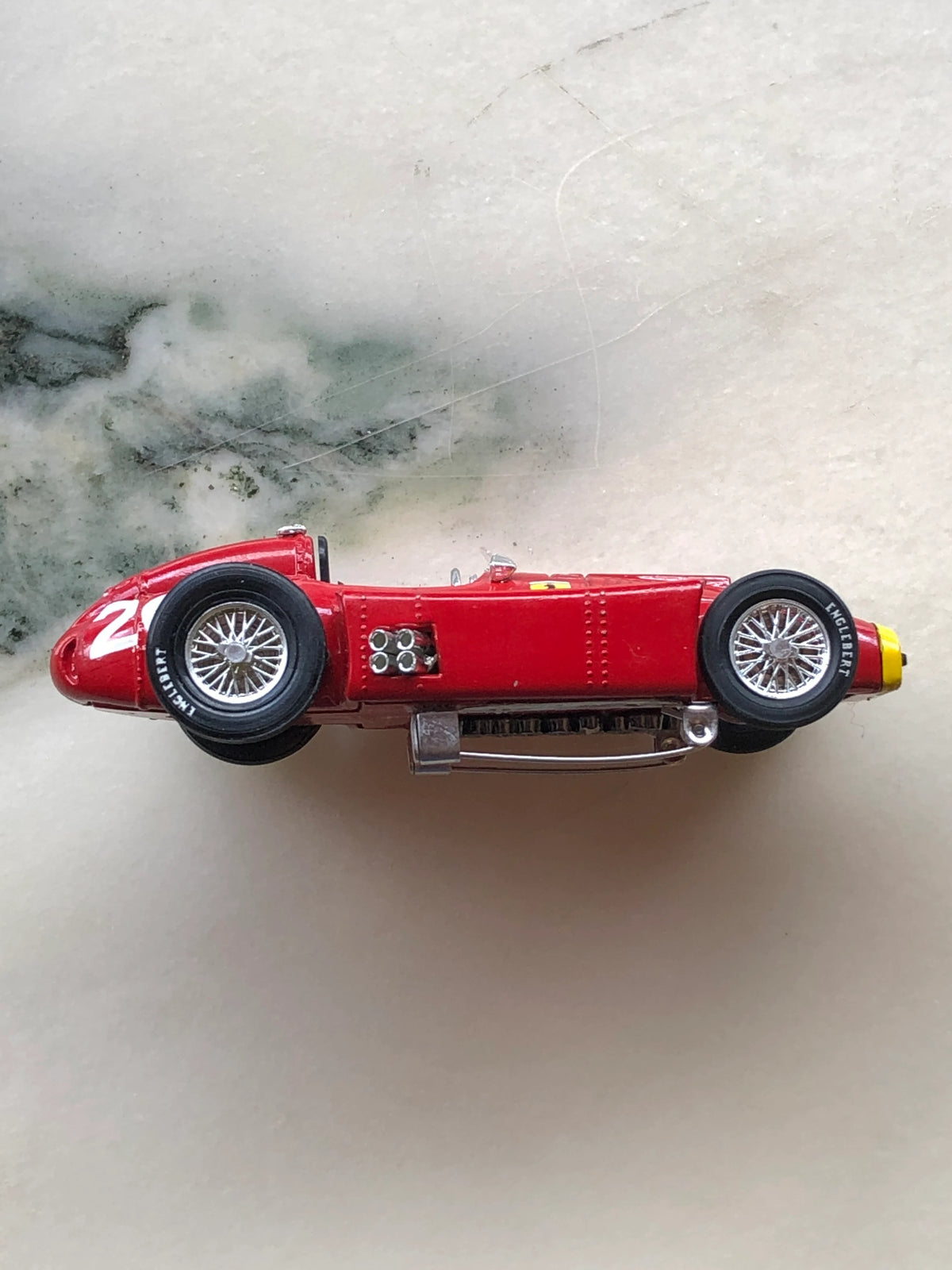 Broochella Men's Rosso Classico No.20 Ferrari Racing Car Brooch in side profile, featuring a vintage red Formula racing car with silver wire-spoke wheels, exposed exhaust pipes, black tyres, yellow nose detailing and a metal brooch pin fastening underneath.