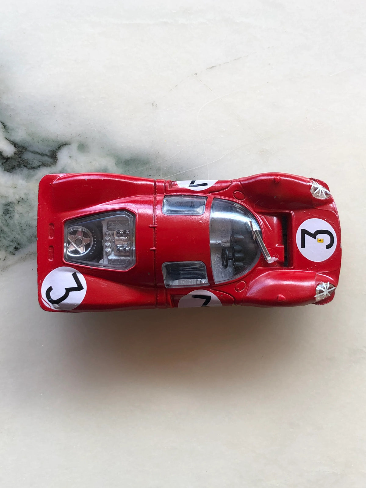 Broochella Men's Rosso Le Mans No.3 Vintage Ferrari Racing Car Brooch viewed from above, showcasing its red bodywork, white number 3 racing decals, transparent cockpit canopy, rear engine detailing and aerodynamic design.