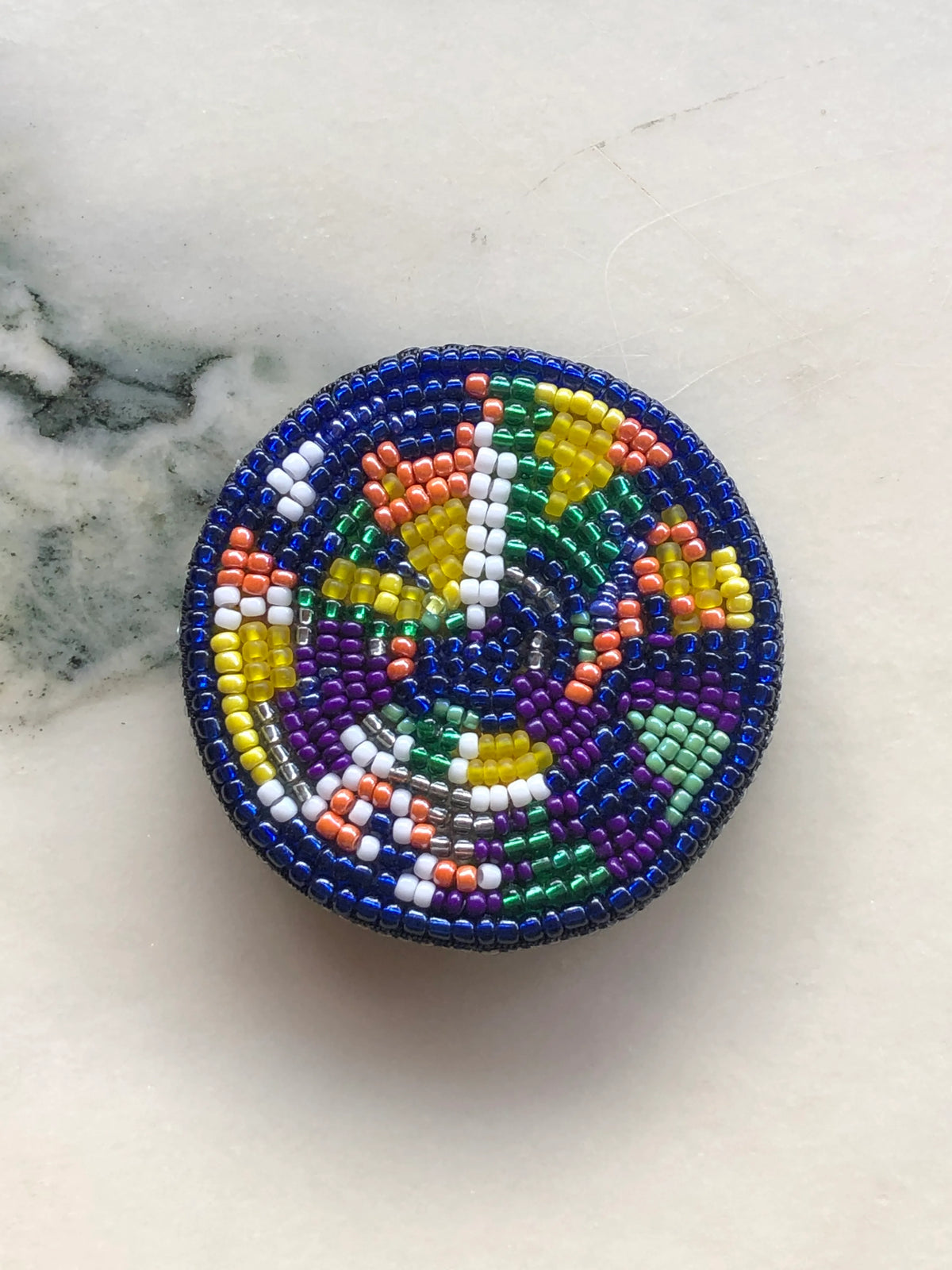 Broochella Men’s Viva La Gioia Brooch Large, hand-beaded in vibrant blue, green, yellow, purple, orange and white beads, photographed on a white marble background.