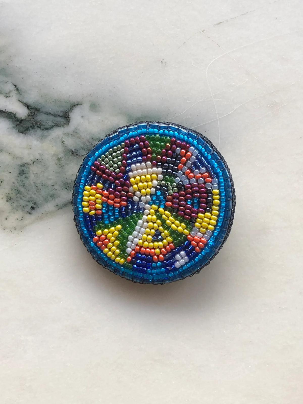 Broochella Men’s Viva La Gioia Brooch Small, hand-beaded in vibrant turquoise, blue, green, yellow, burgundy, orange and white beads, photographed on a white marble background.