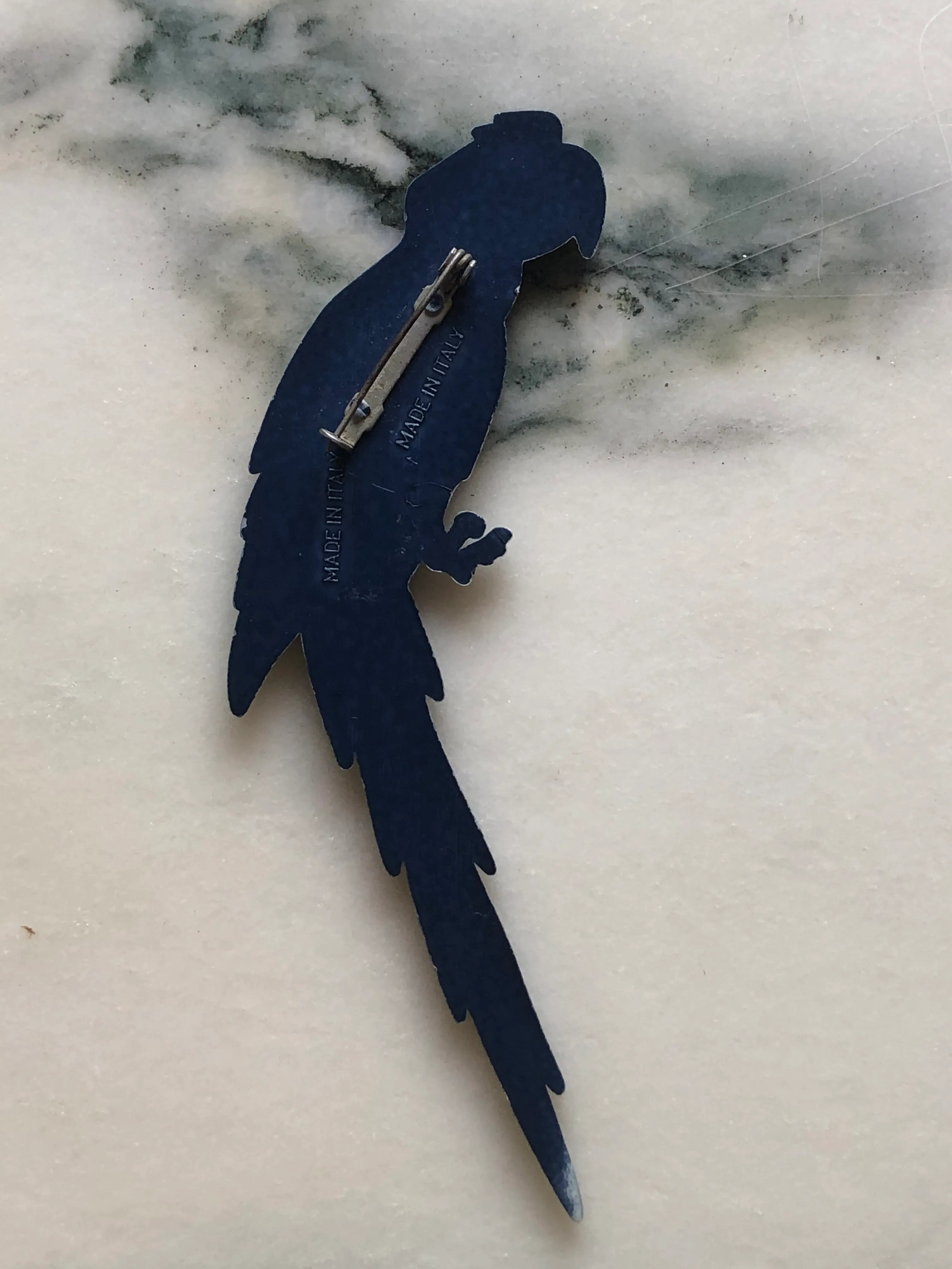 Broochella Midnight Macaw vintage Italian parrot brooch in deep blue with a clear crystal eye, sculpted wings and a long feathered tail, measuring approximately 13.5 × 5 cm. Photographed on white and grey marble.