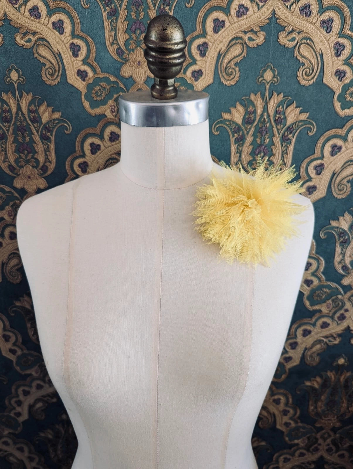 Broochella monello handmade tulle urchin brooch in yellow. The brooch is pinned on a mannequin. The background is green and gold damask wallpaper.