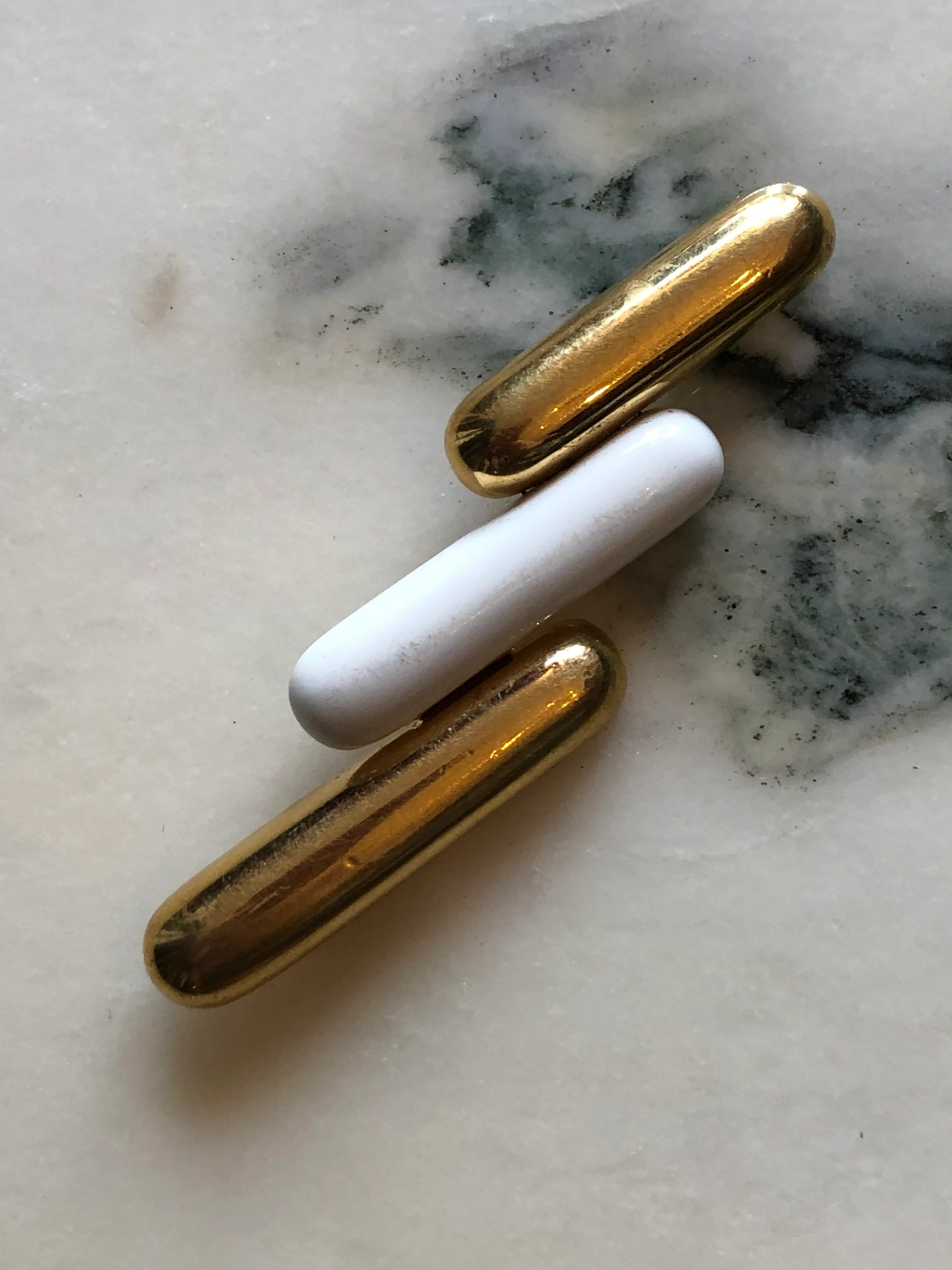Broochella Monet Vintage Directives brooch with three elongated gold-tone and ivory enamel geometric bars. The background is white marble.