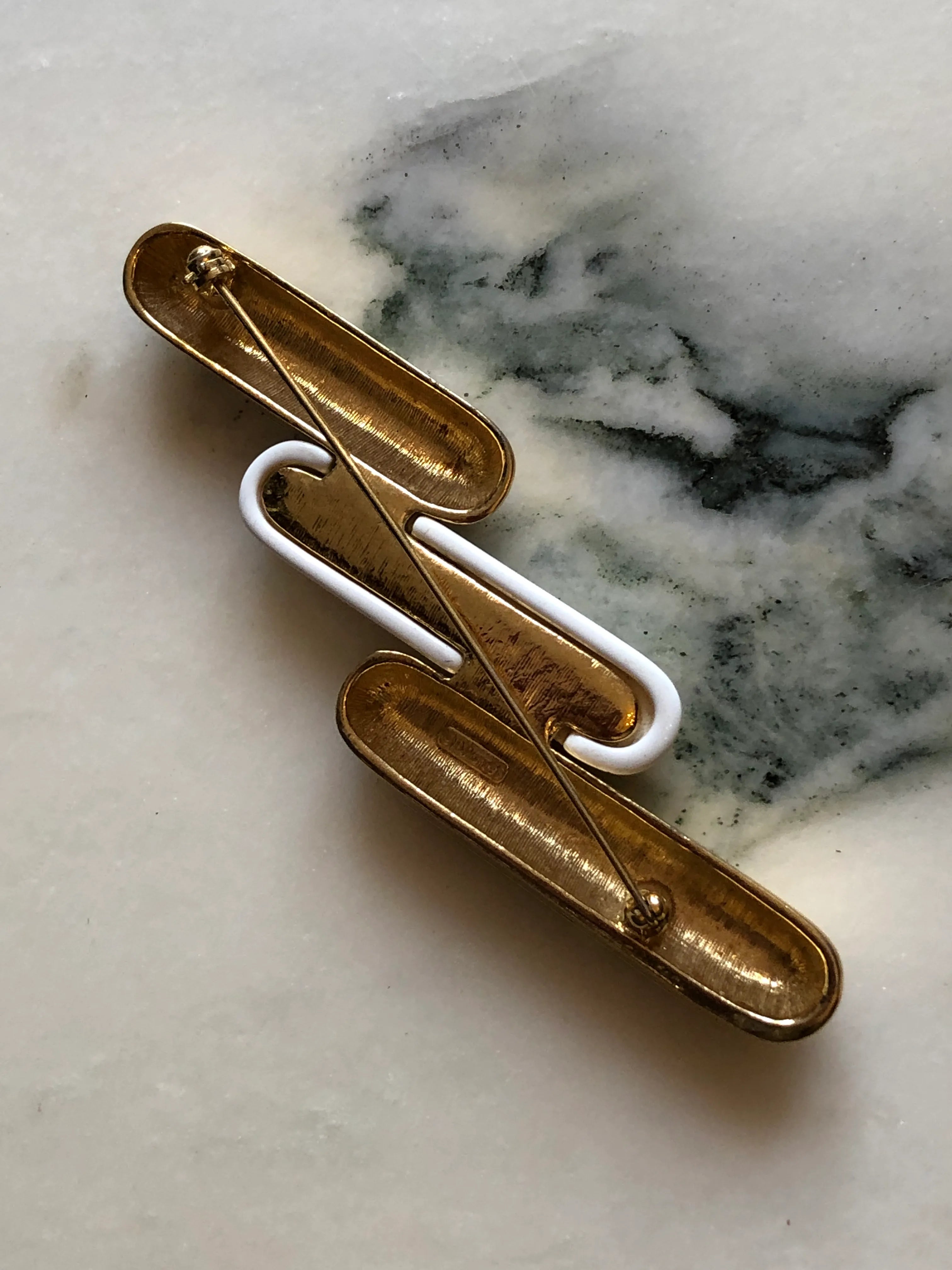 Broochella Monet Vintage Directives brooch with three elongated gold-tone and ivory enamel geometric bars. The background is white marble