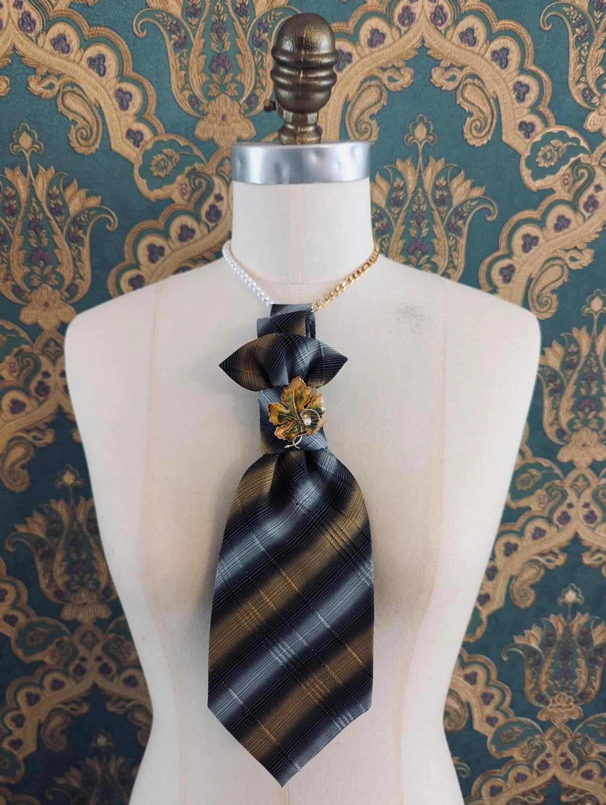 Broochella Montecristo cravatta vintage yellow  and grey striped handmade up cycled tie brooch with vintage brooch embellishment. It is pinned to a mannequin The background is green and gold damask wallpaper. 