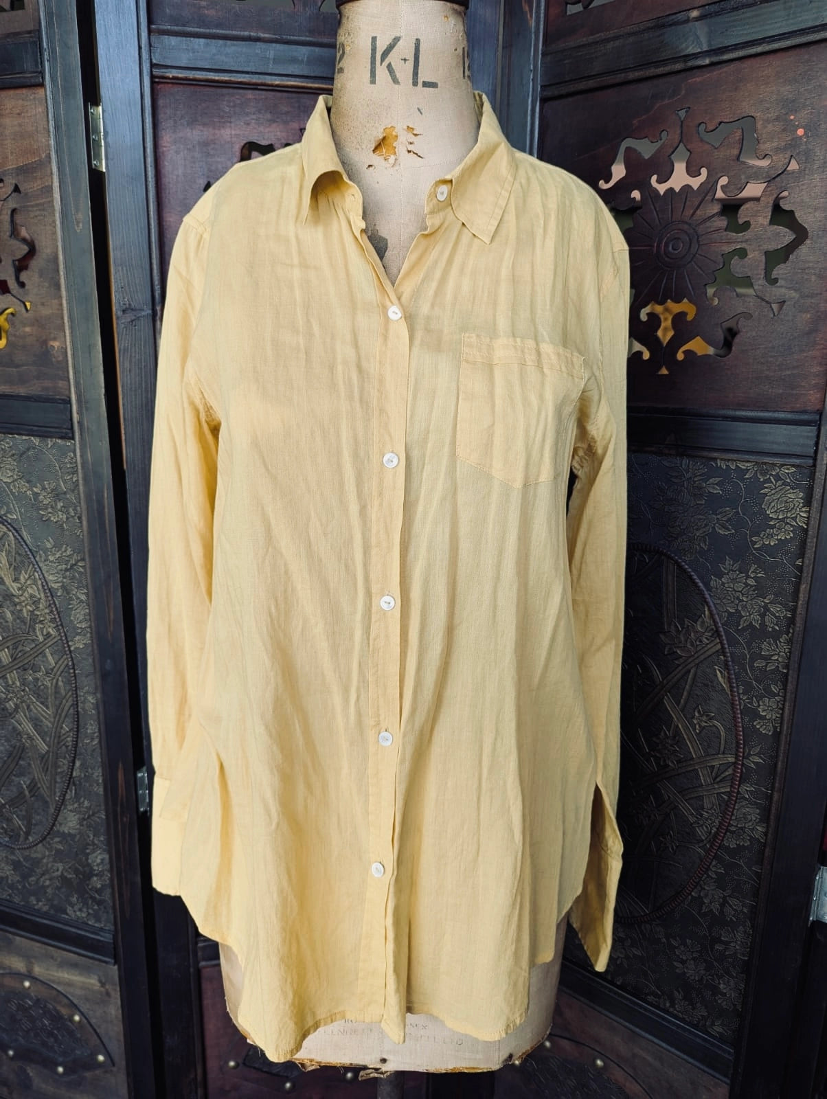 Nili Lotan Cotton Mustard Yellow Button-Up Shirt – Size L. It is pictured on a vintage mannequin. The background is an ornate dark wood screen. 