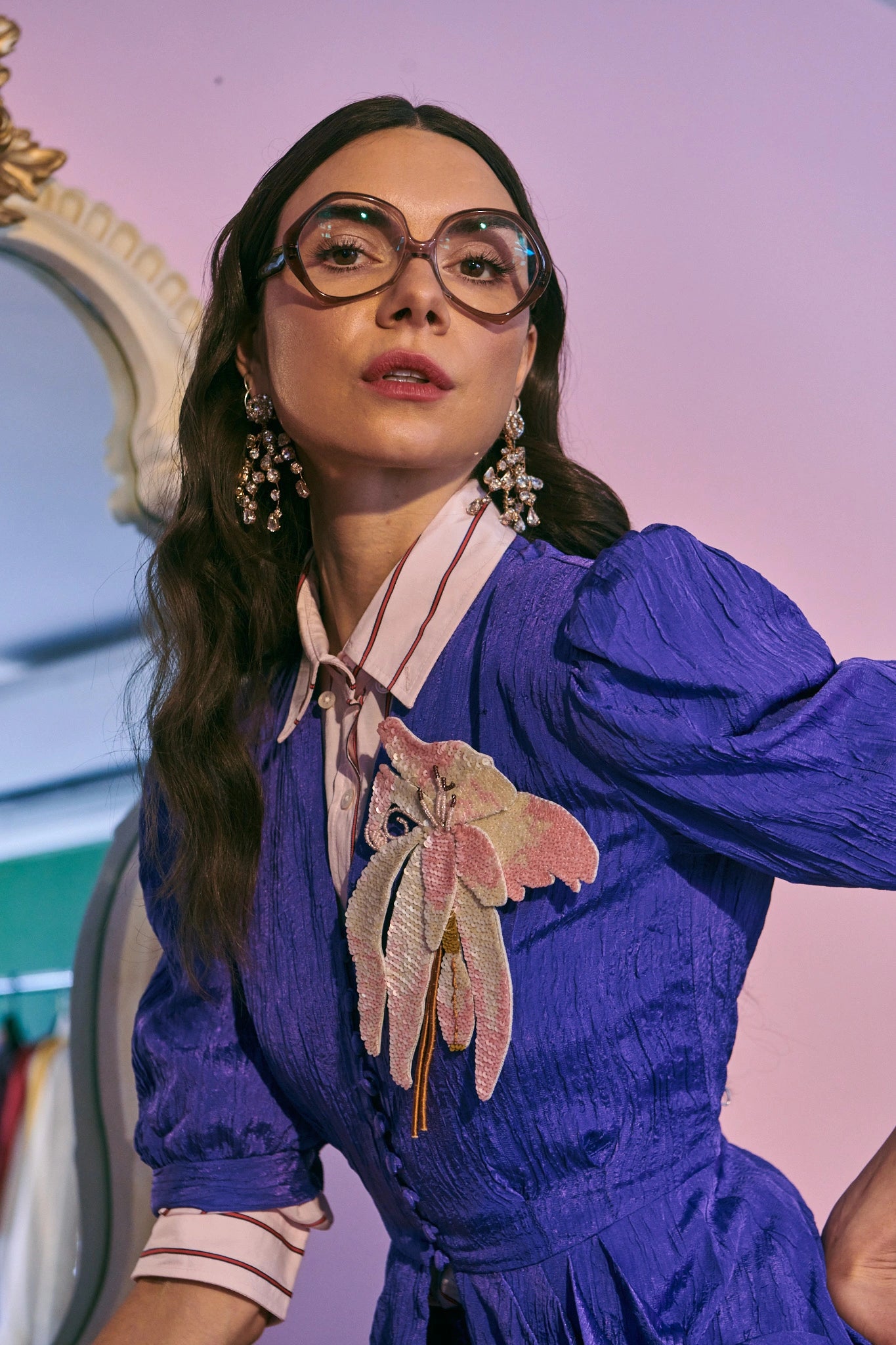 Broochella orchid ingioiellato flower brooch pictured on a model. She is wearing a purple dress. The background is  pink. 