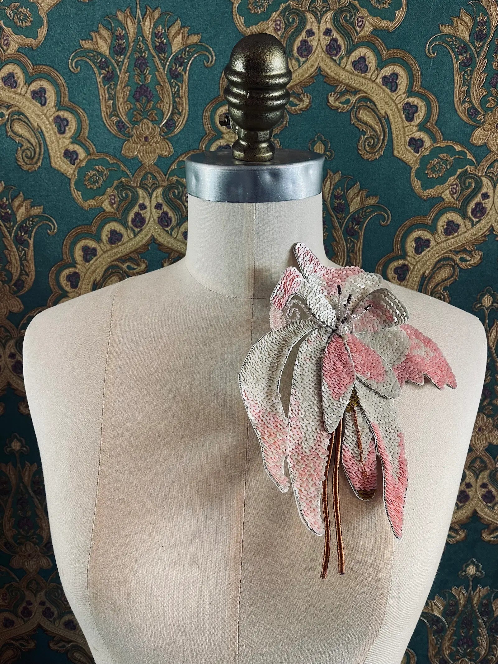 Broochella orchid ingioiellato large hand beaded pink and white flower brooch. Pictured on a mannequin. The background is green and gold damask wallpaper