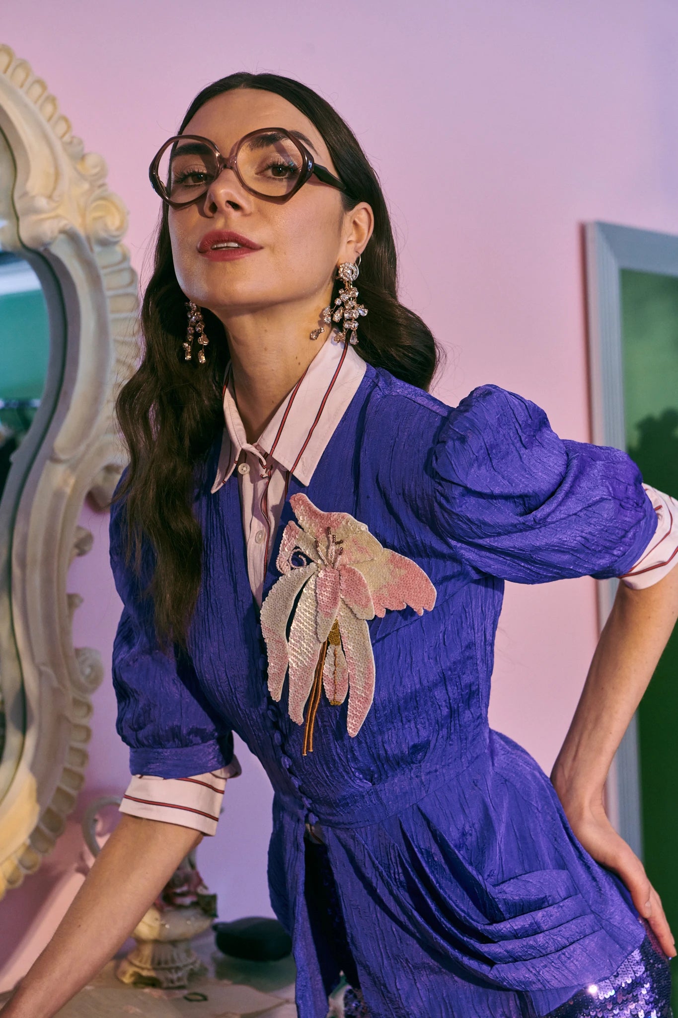 Broochella orchid ingioiellato flower brooch pictured on a model. She is wearing a purple dress. The background is  pink. 