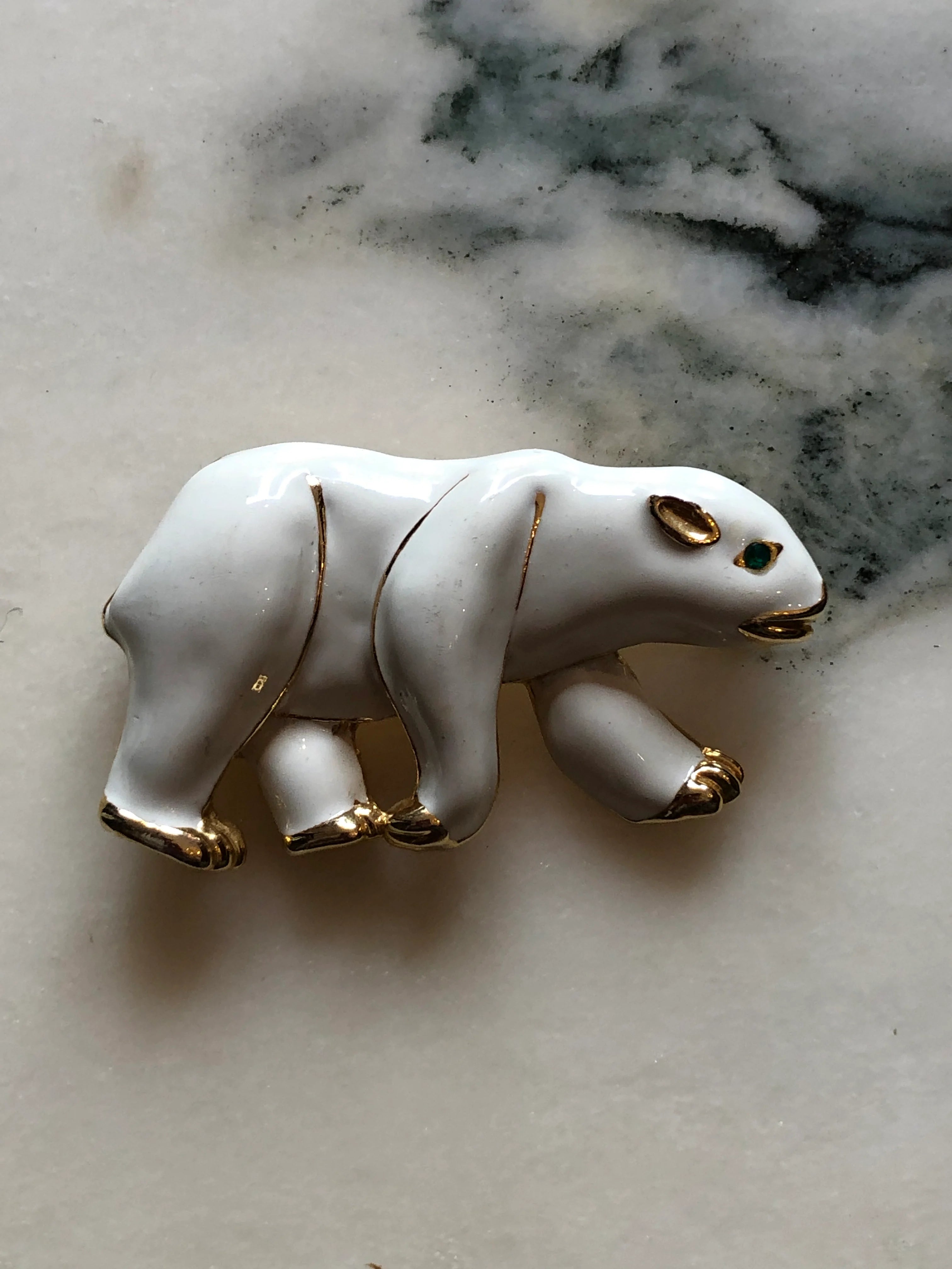 Broochella Orso Bianco vintage white enamel polar bear brooch with gold-tone details and a green crystal eye. The background is white marble