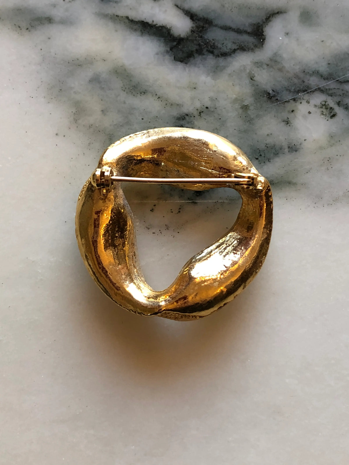 Broochella Ottavia Vintage Black & Crystal Swirl Brooch featuring black and clear crystals set into a sculptural gold-tone circular design on a cream and grey marble background.