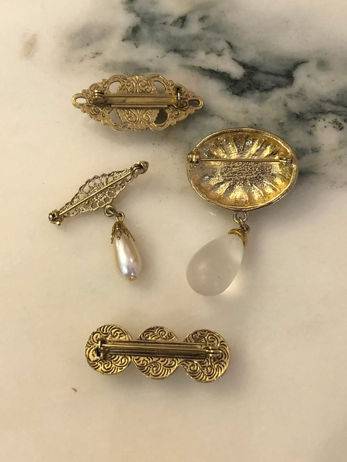 Broochella The Perla Vintage Brooch Quartet featuring four ivory faux-pearl, filigree and gold-tone vintage brooches.  The background is white marble.