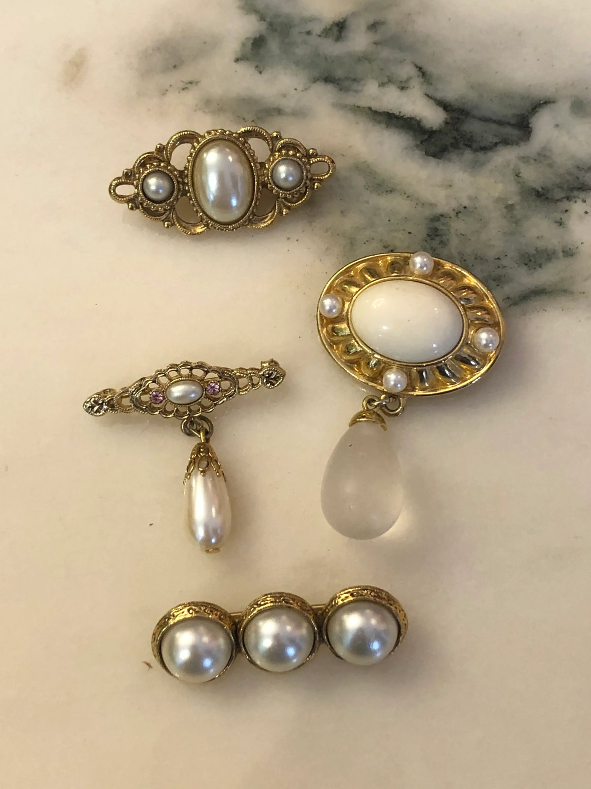 Broochella The Perla Vintage Brooch Quartet featuring four ivory faux-pearl, filigree and gold-tone vintage brooches.  The background is white marble.