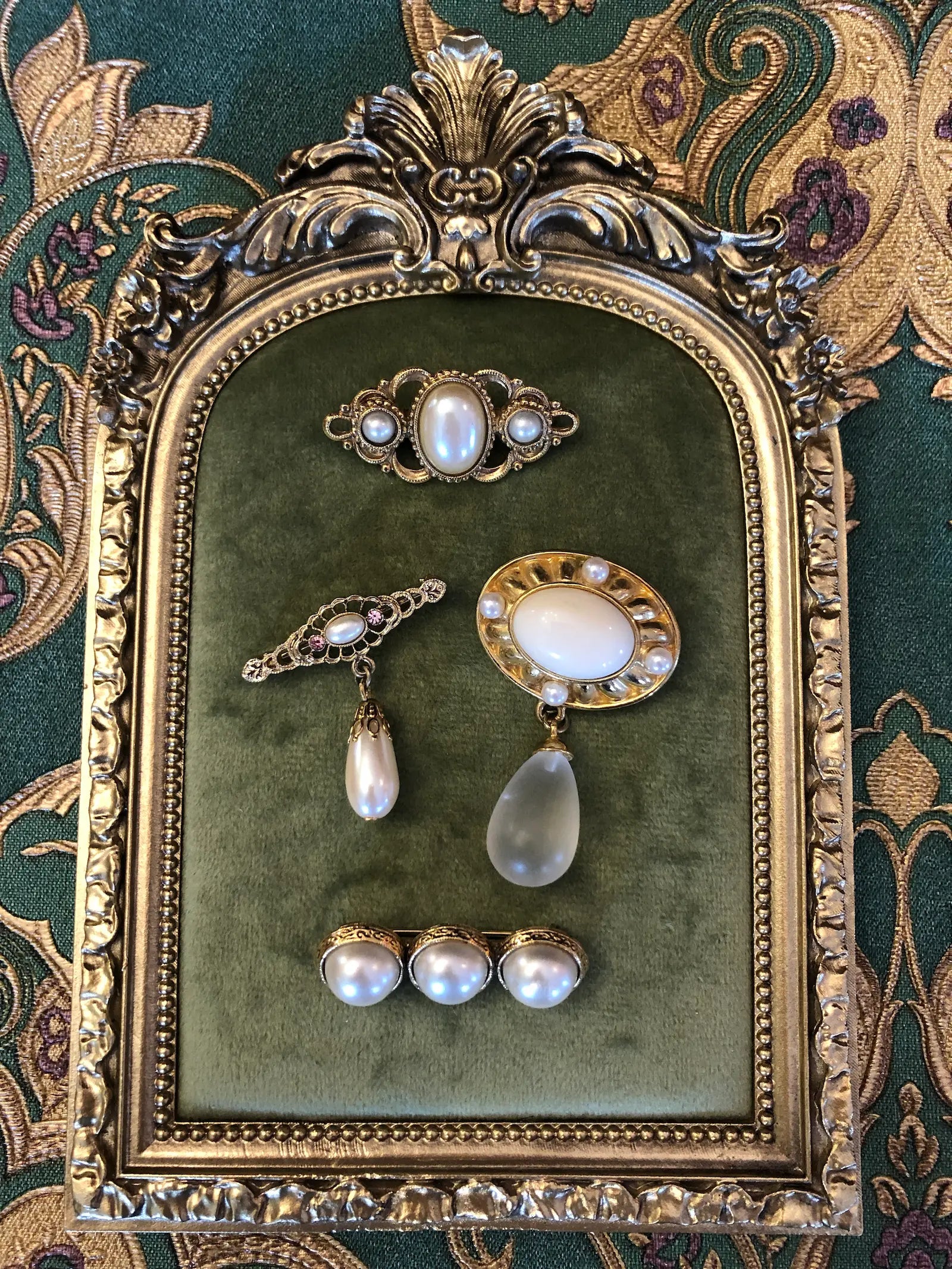 Broochella The Perla Vintage Brooch Quartet featuring four ivory faux-pearl, filigree and gold-tone vintage brooches. They are displayed on a green marble tray. The background is green and gold damask wallpaper. 