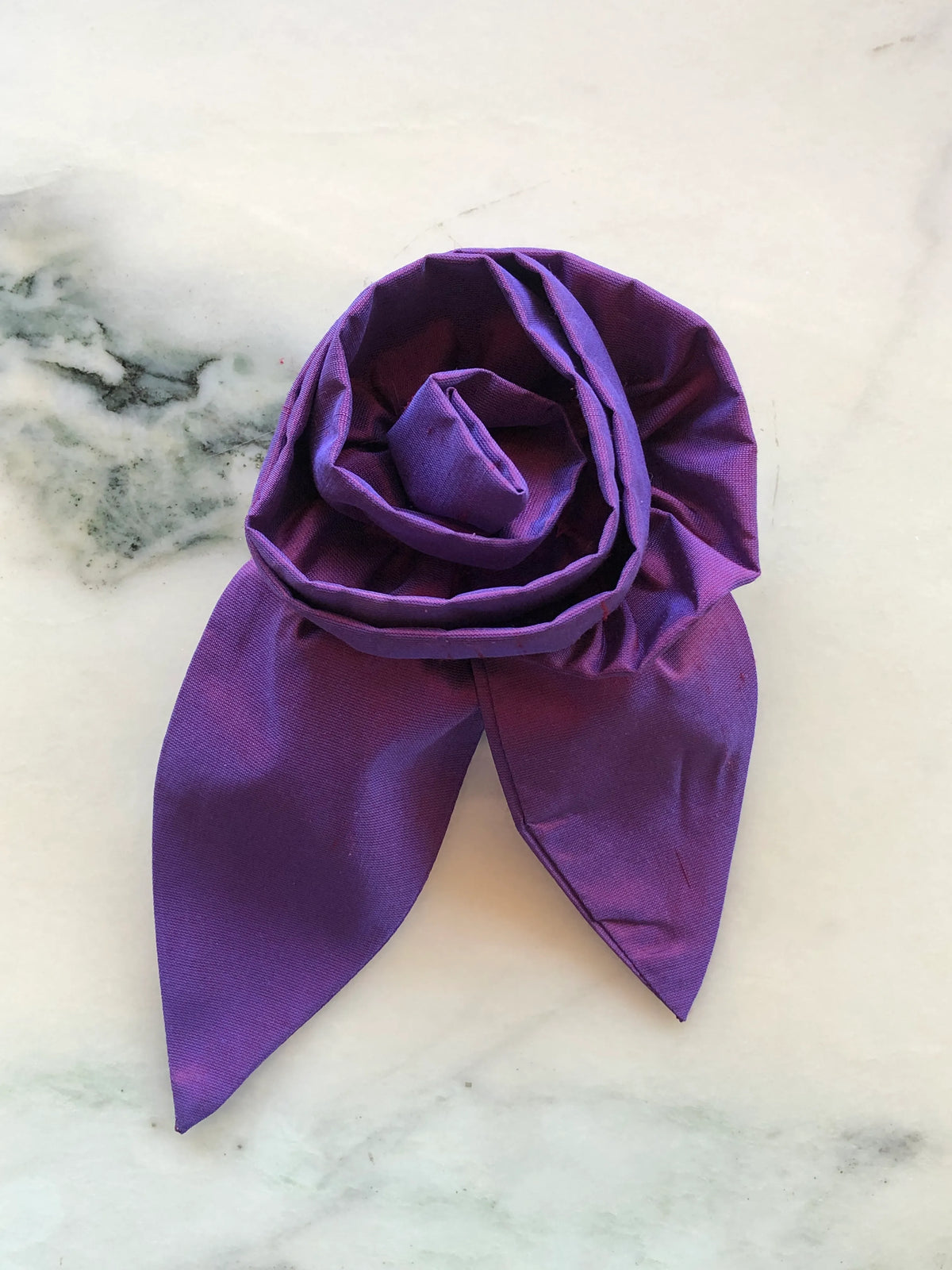 Broochella Petalo Large purple silk flower brooch with sculptural rose petals and two pointed silk leaves, photographed on white marble with grey-green veining.
