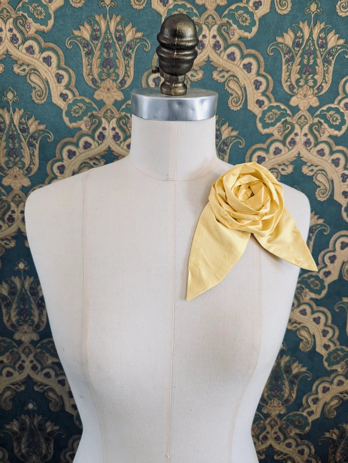 Broochella Petalo handmade silk flower brooch with petal detail in yellow. Pinned to a mannequin. The background is green and gold damask wallpaper.