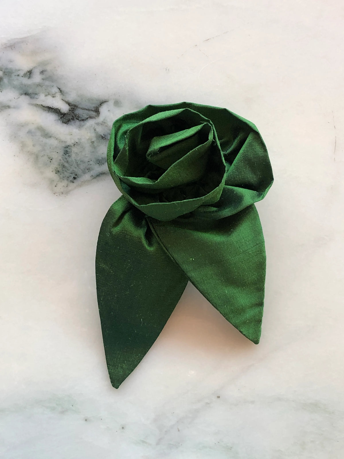 Broochella Petalo Small green silk flower brooch with sculptural rose petals and two pointed silk leaves, photographed on white marble with grey-green veining.