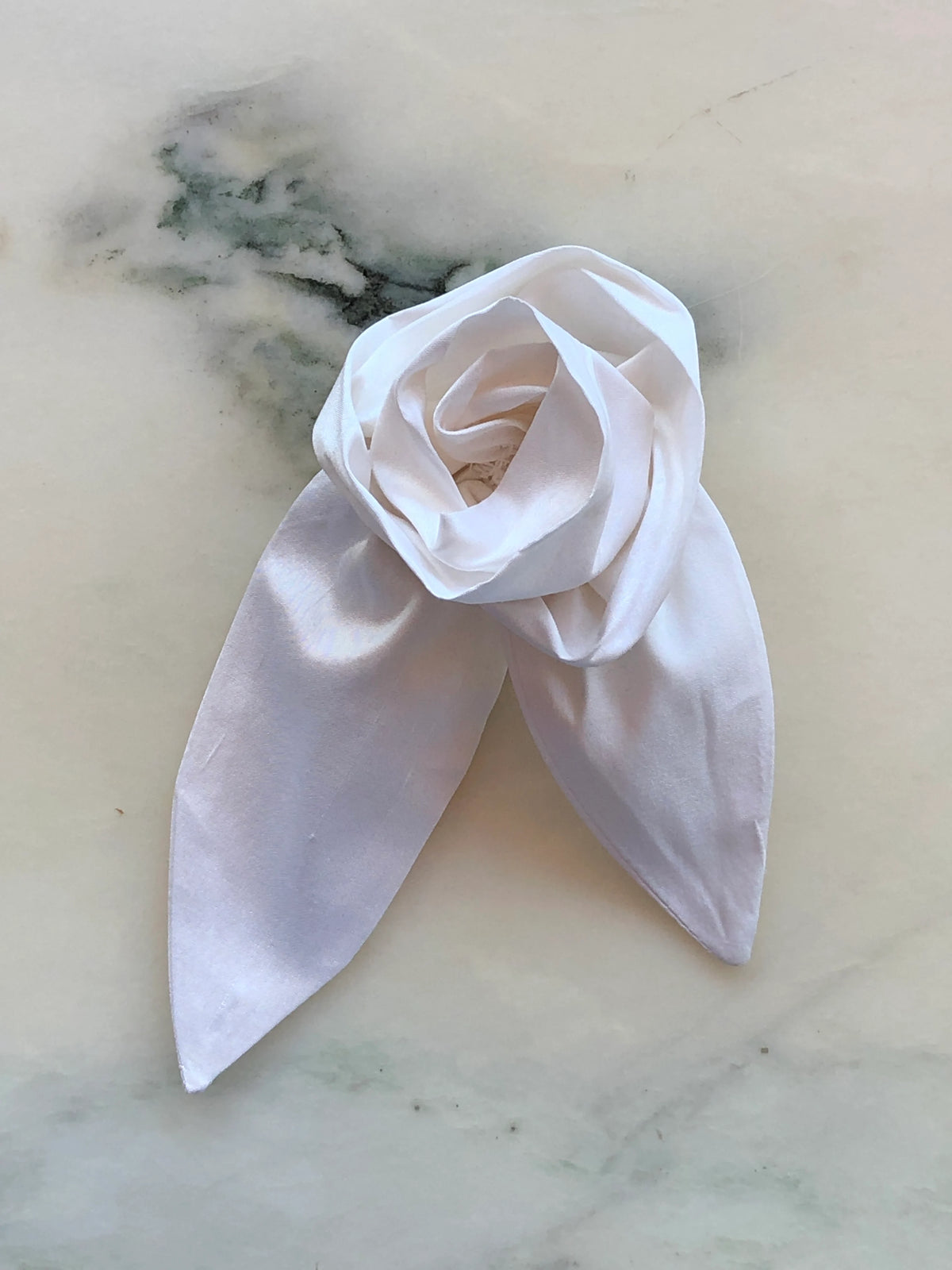 Broochella Petalo Men ivory silk flower brooch for men with sculptural rose petals and two pointed silk leaves, photographed on white marble with grey-green veining.