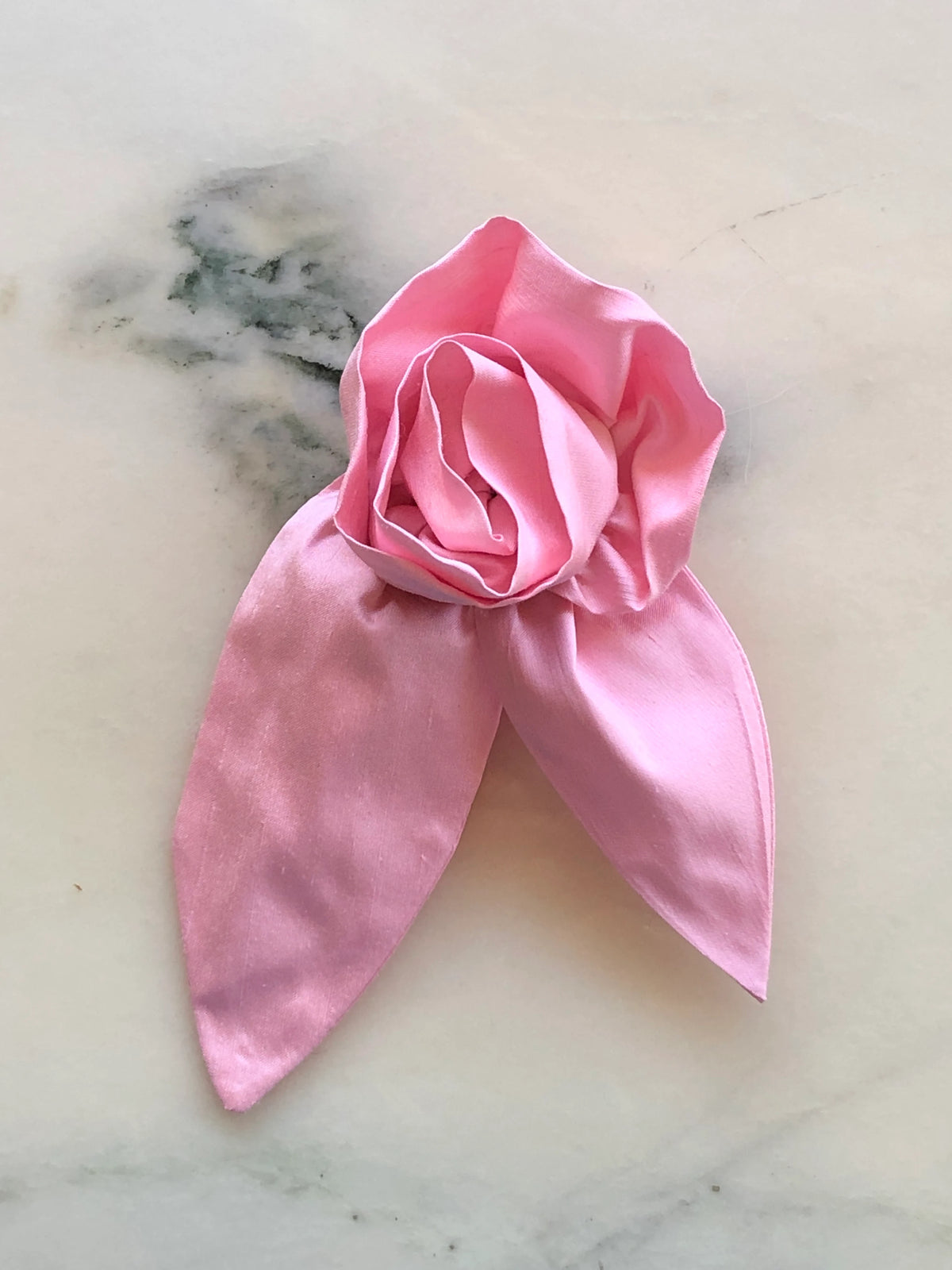 Broochella Petalo Men pink silk flower brooch for men with sculptural rose petals and two pointed silk leaves, photographed on white marble with grey-green veining.