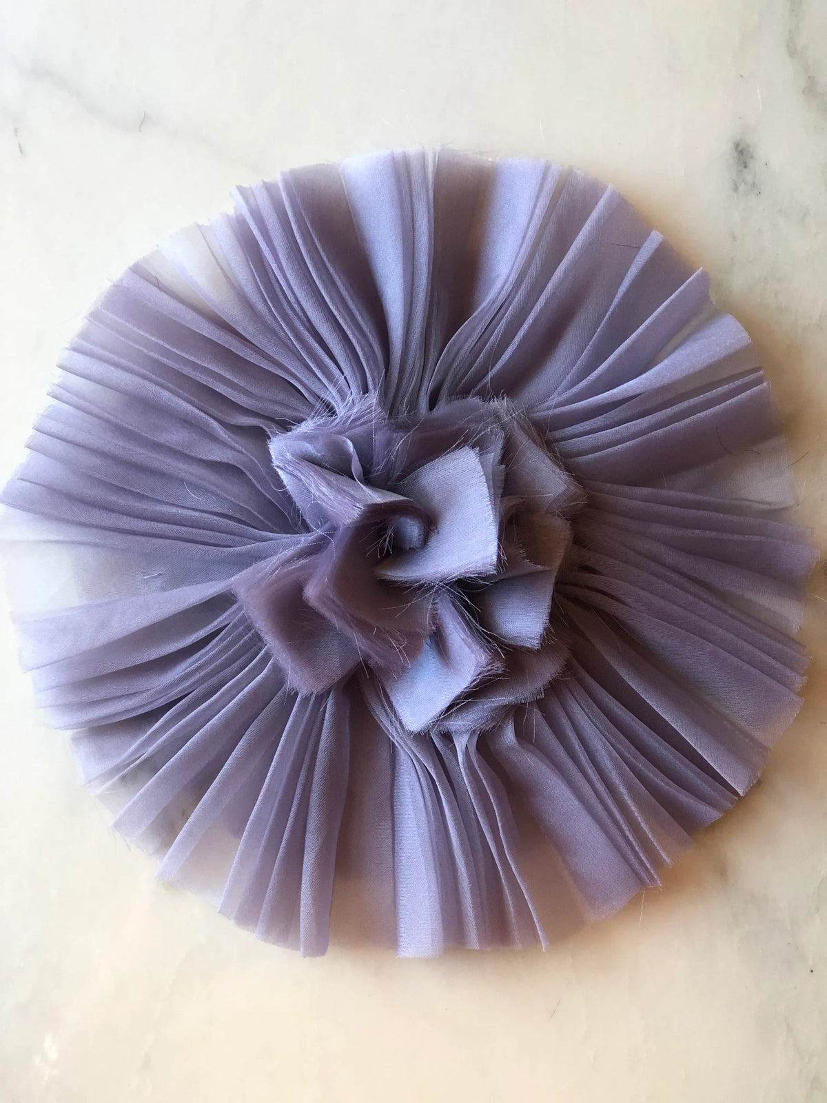 Broochella Men's Pieghettato Large Organza Flower Brooch Pin in soft lavender, featuring pleated organza petals arranged in a circular design with a softly frayed sculptural centre on a marble background.