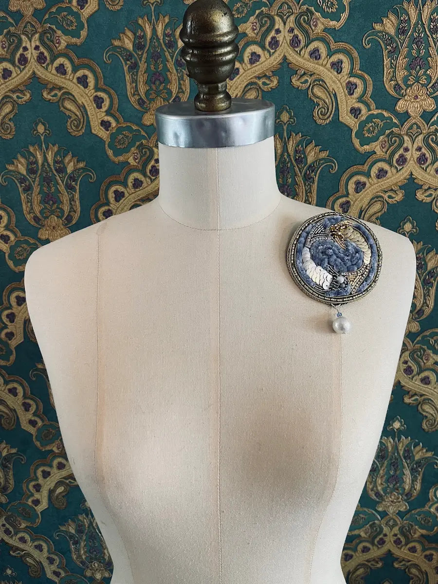 Broochella pisces zodiac hand beaded designer brooch. Styled on a mannequin. The background is green and gold damask wallpaper