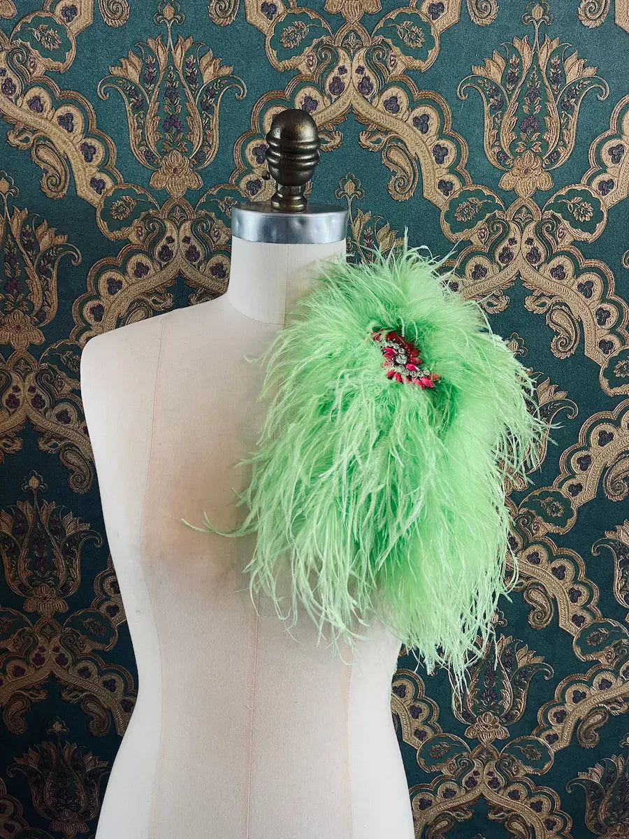 Broochella Piuma handmade neon green feathered embellished designer brooch pictured on a mannequin the background is green and gold damask wallpaper