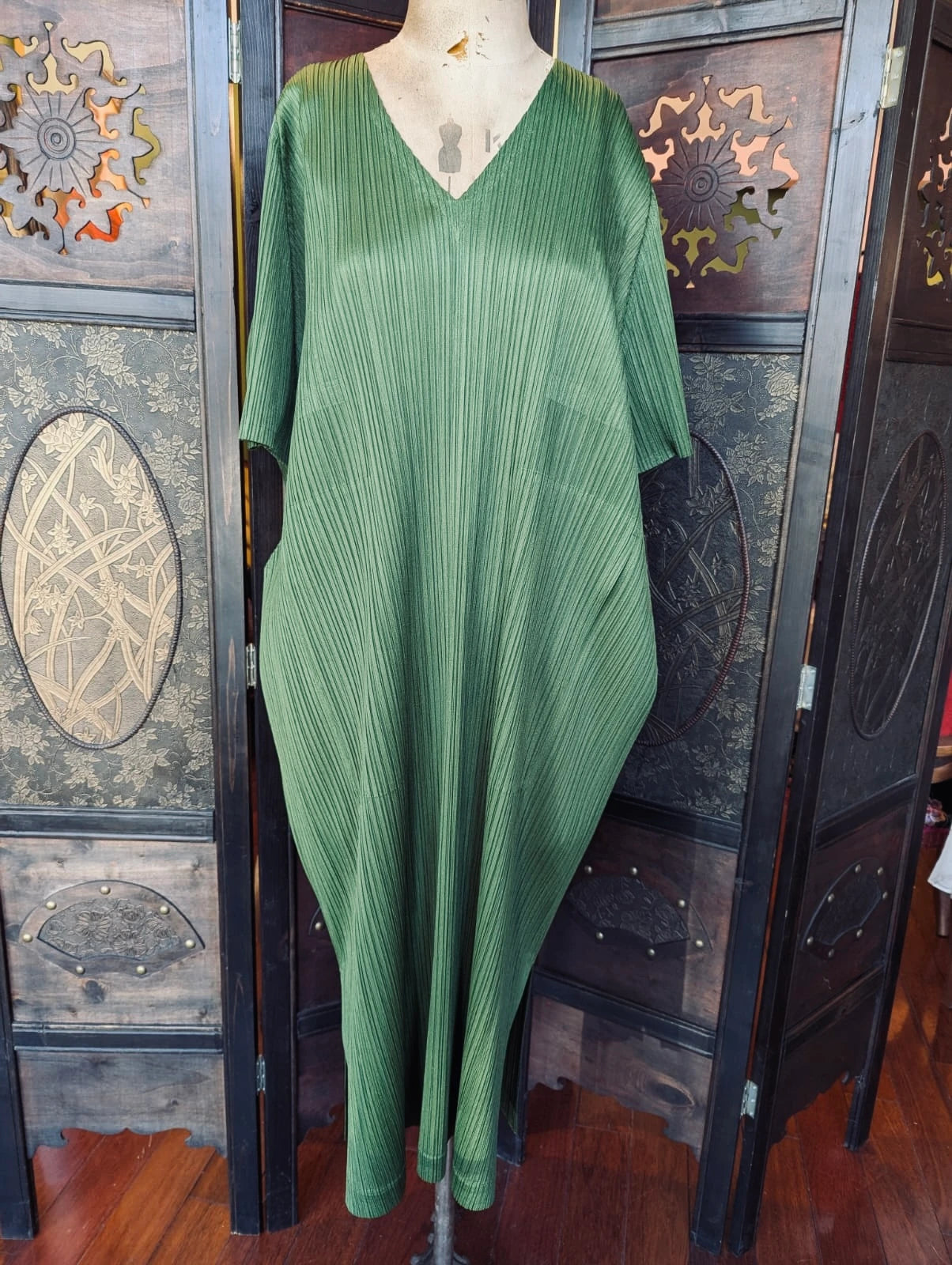 A Broochellaauthentic designer  Issey Miyake Pleated Please green pleated kaftan maxi dress displayed on a mannequin torso, set against a dark wooden folding screen.