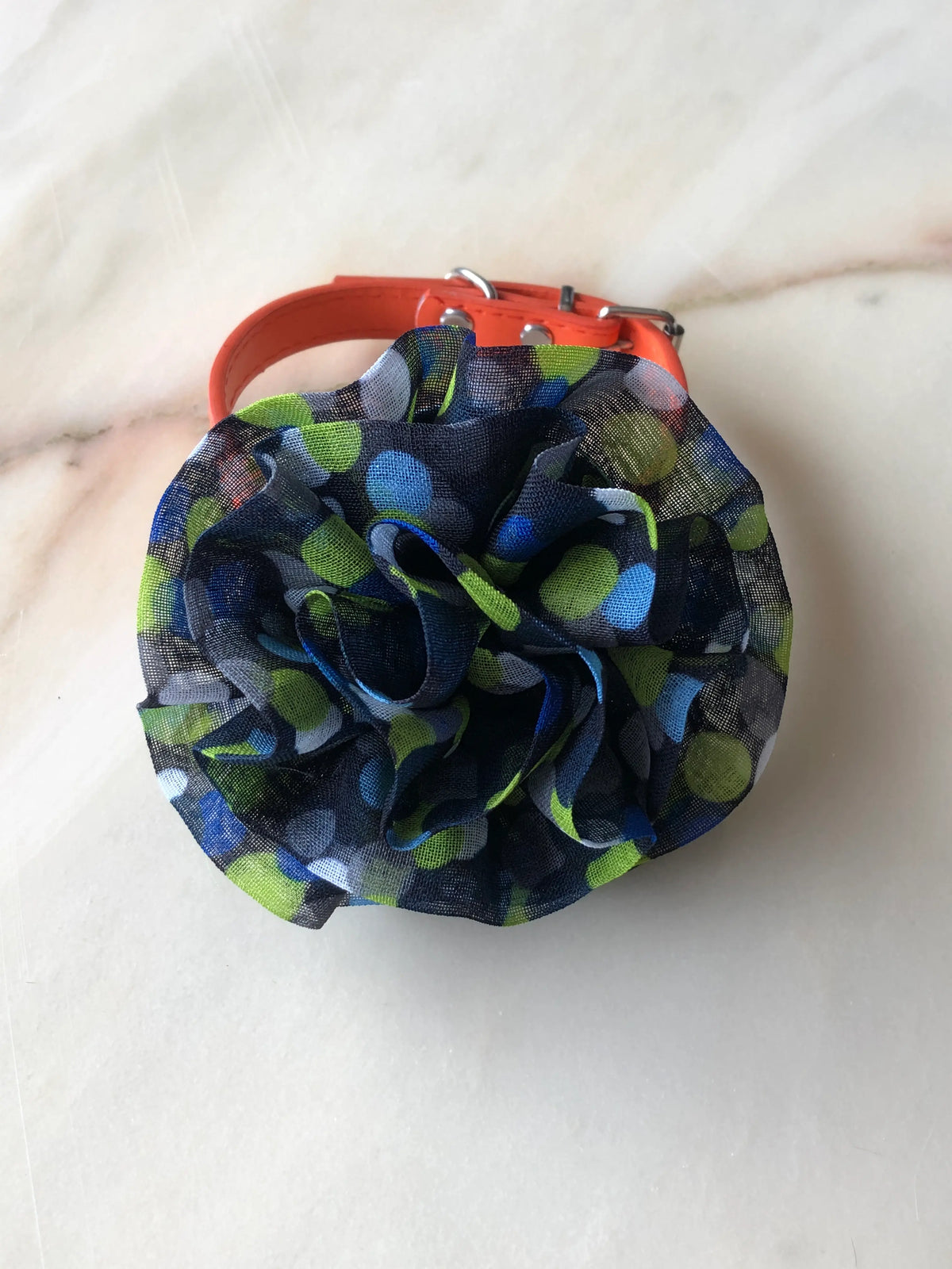 Broochella Poochella Brassica blue pet flower featuring a sculptural rosette of gathered sheer navy mesh with lime-green, cobalt-blue, pale-blue and grey polka dots, photographed from above on cream marble with subtle grey veining.