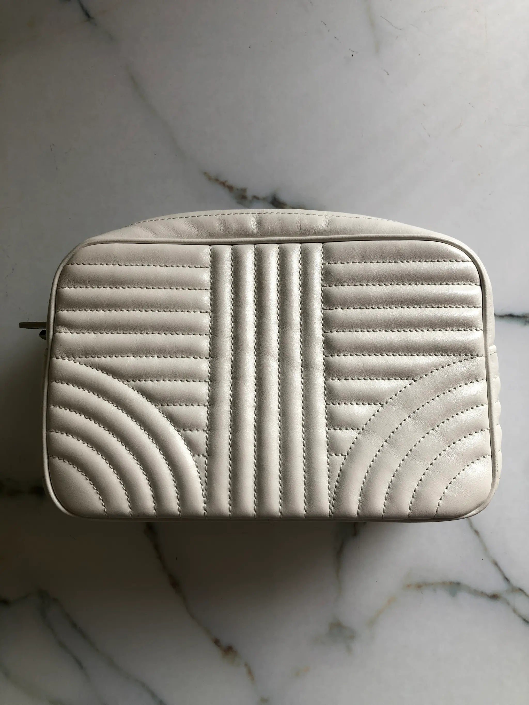 A cream-coloured quilted Broochella Prada bag with a geometric stitched pattern, shown from a top-down view on a white marble surface.
