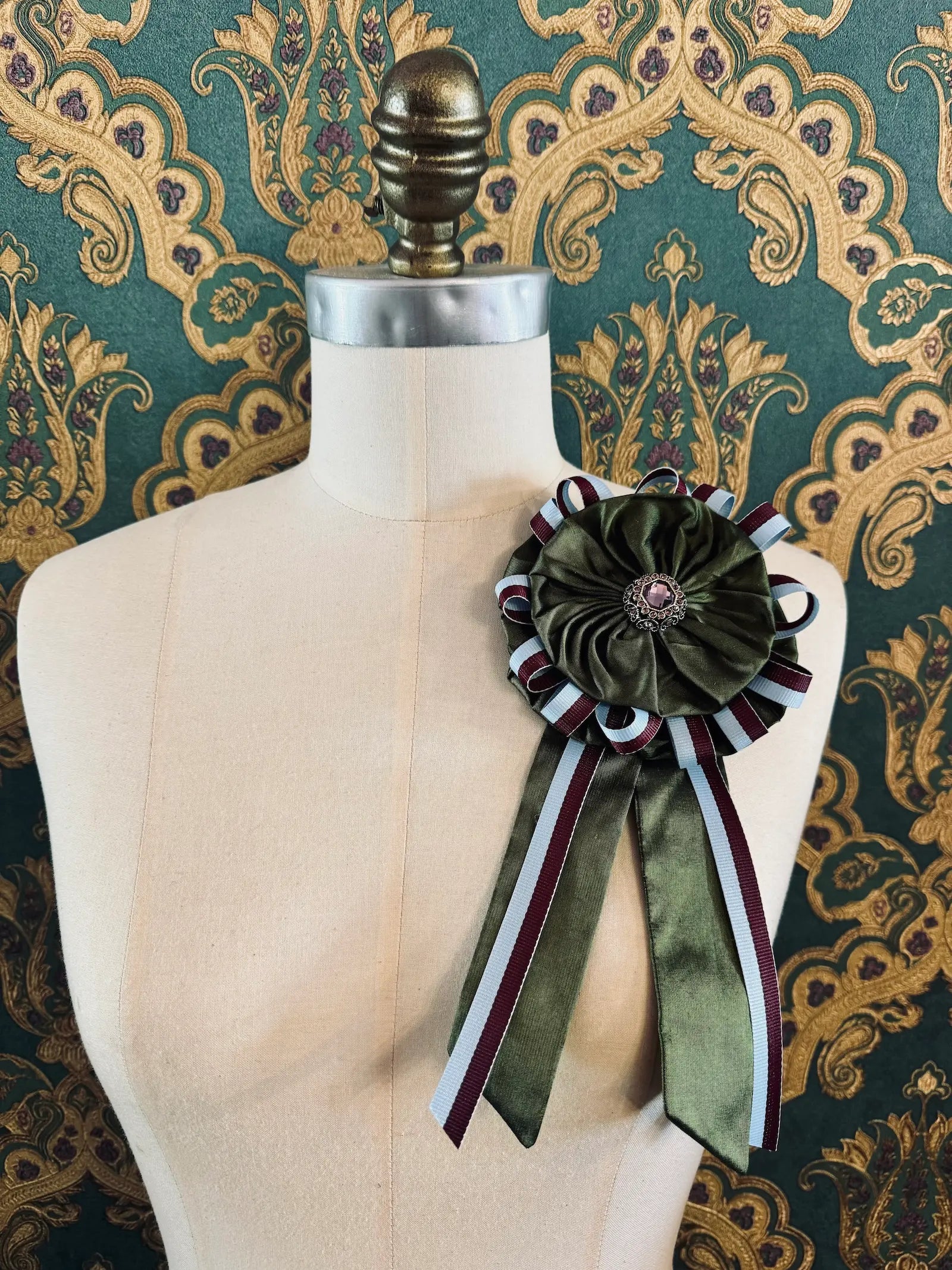 Broochella regalia silk ribbon brooch with vintage ribbon trim in green. Pictured on a mannequin. The background is green and gold damask wallpaper.