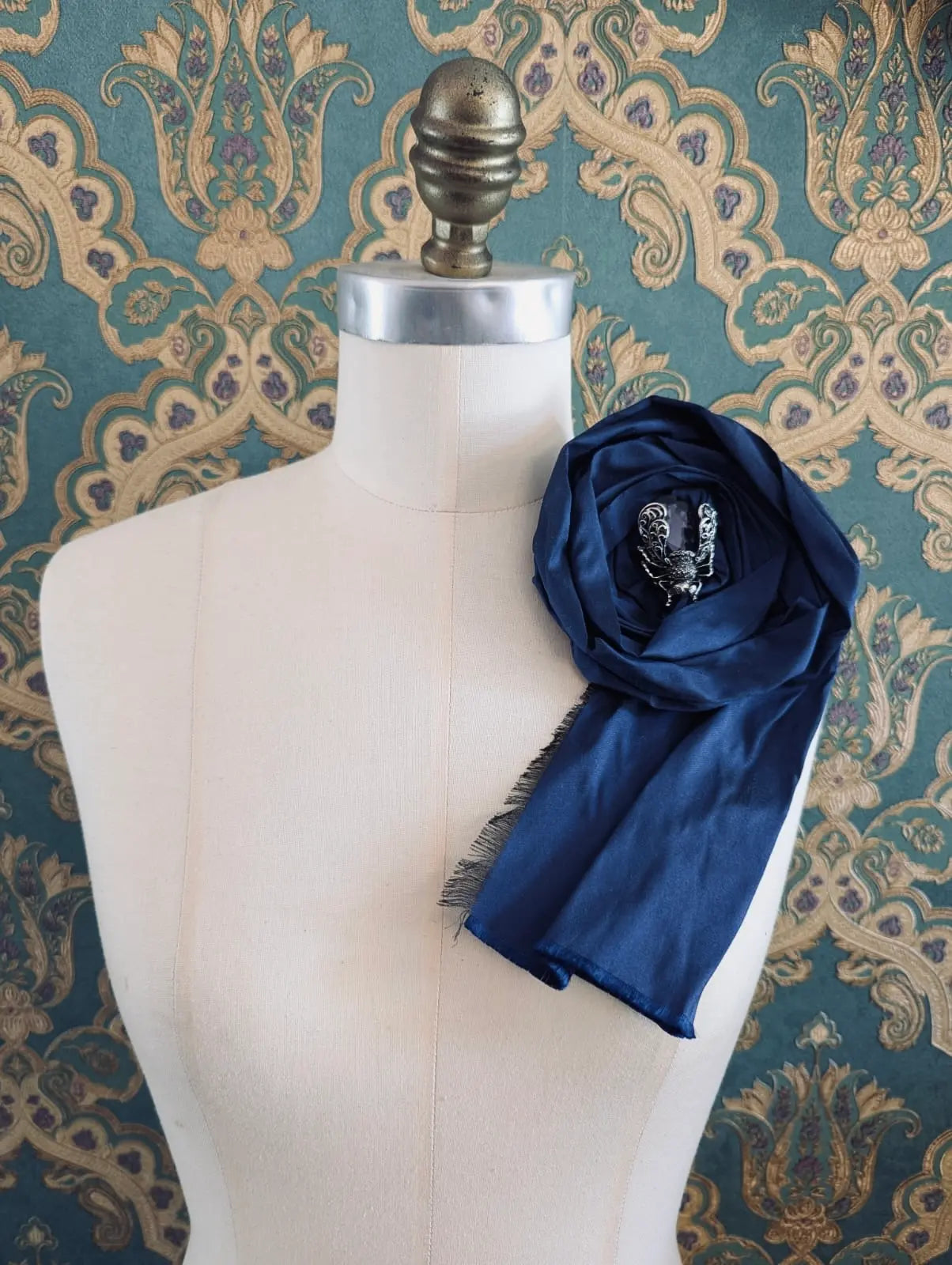 Broochella rosa ingioiellata navy handmade designer silk silk flower brooch with rhinestone insect embellishment. styled on a mannequin. The background is green and gold damask wallpaper