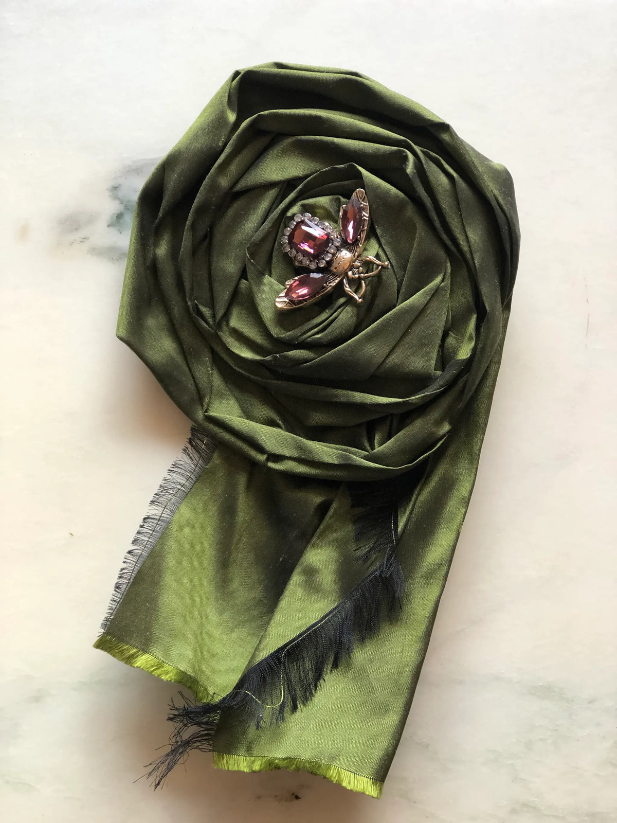 Broochella Rosa Ingioiellata Flower Brooch Pin - Small in rich green silk, styled with a vintage blue crystal and silver-tone brooch at its centre on a cream marble background.