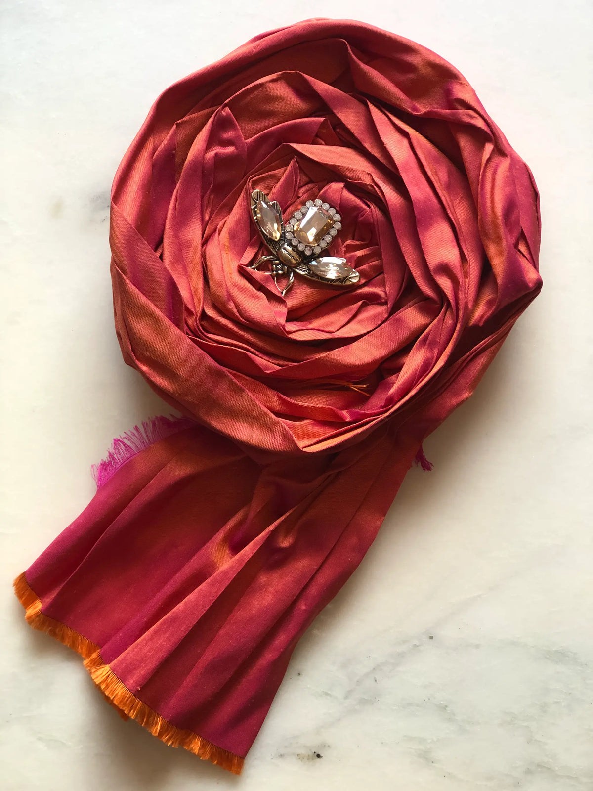 Broochella Rosa Ingioiellata Flower Brooch Pin - Small in rich tangerine silk, styled with a vintage blue crystal and silver-tone brooch at its centre on a cream marble background.