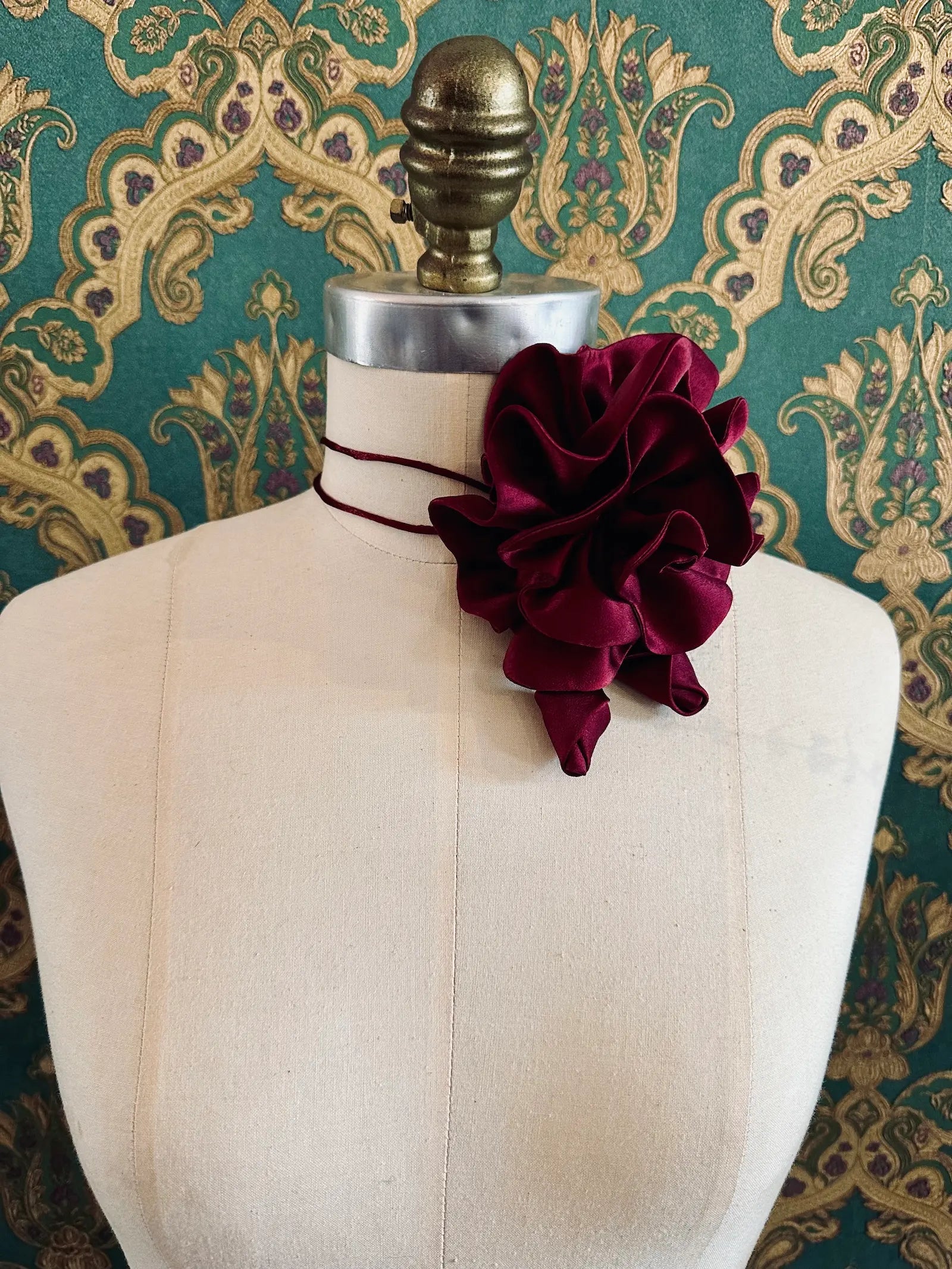 Broochella Rosetta burgundy handmade silk satin flower brooch and choker  Pictured on a mannequin. The background is green and gold damask wallpaper