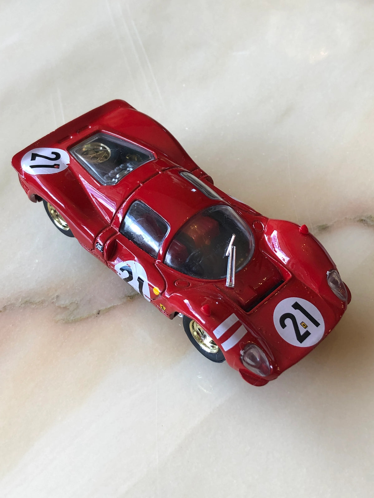 Broochella Rosso Fiorentino No.21 Endurance Racing Car Brooch from the Men’s Collection, featuring a glossy red vintage race car with white number 21 decals, gold wheels, enclosed cockpit and detailed racing bodywork, photographed from an elevated angle.