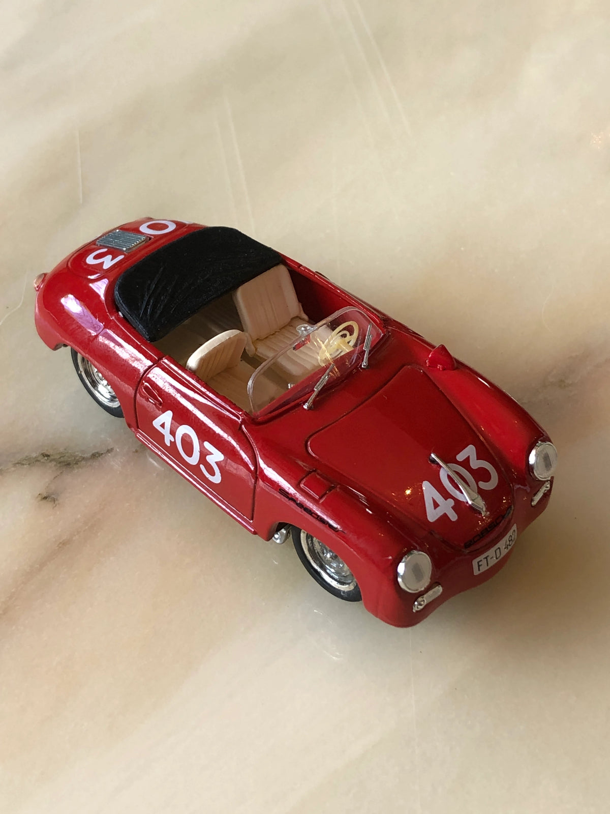 Broochella Rosso Mille No.403 Vintage Convertible Racing Car Brooch in glossy red, featuring white number 403 racing decals, cream leather-look seats, black folded soft top, clear windscreen and silver wheels, photographed from an elevated angle.