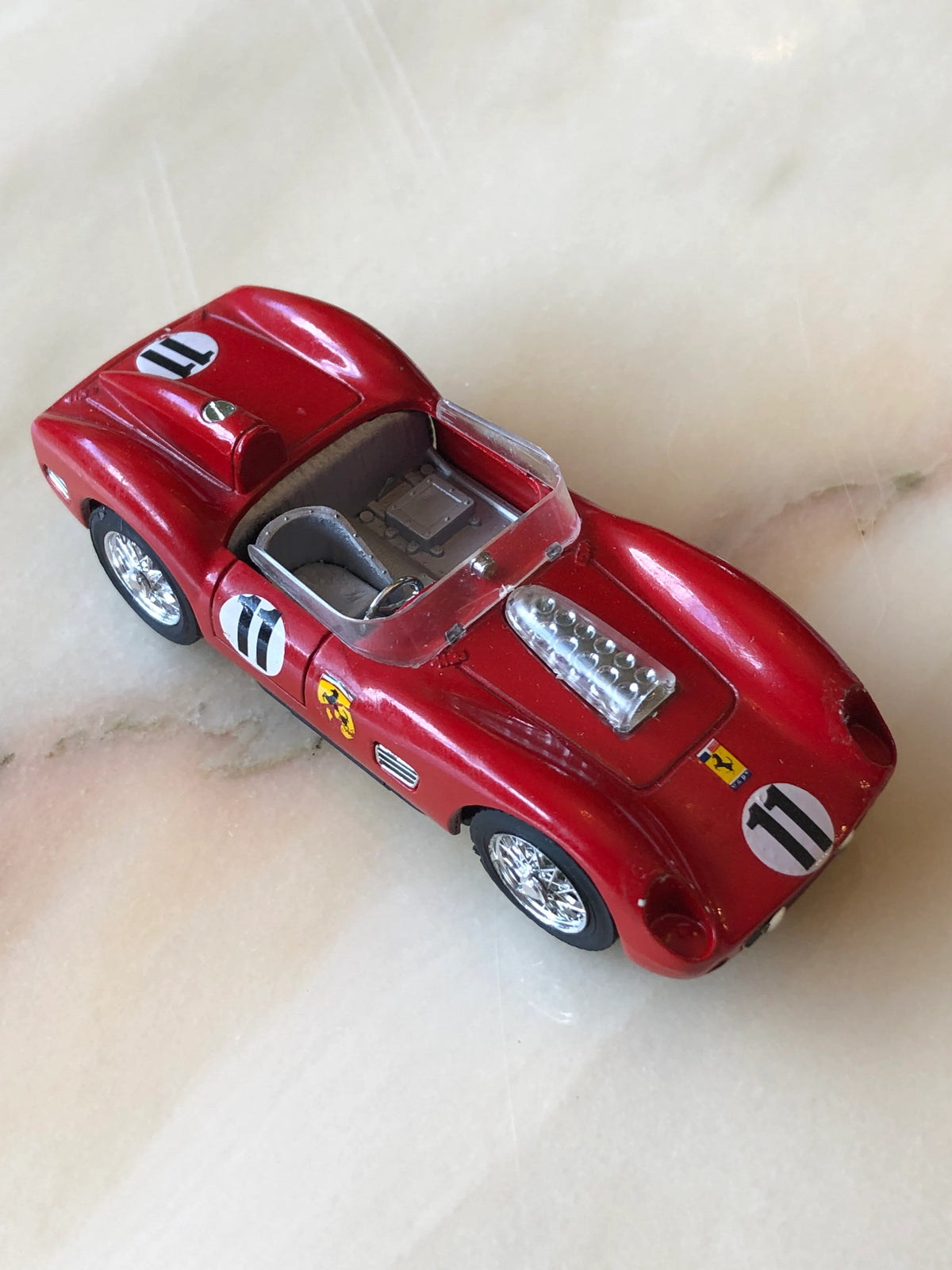 Broochella Rosso Sprint No.11 Vintage Open-Top Racing Car Brooch in glossy red with Ferrari-style racing decals, number 11, silver engine detailing, open cockpit and chrome wire-spoke wheels, photographed at an elevated angle.