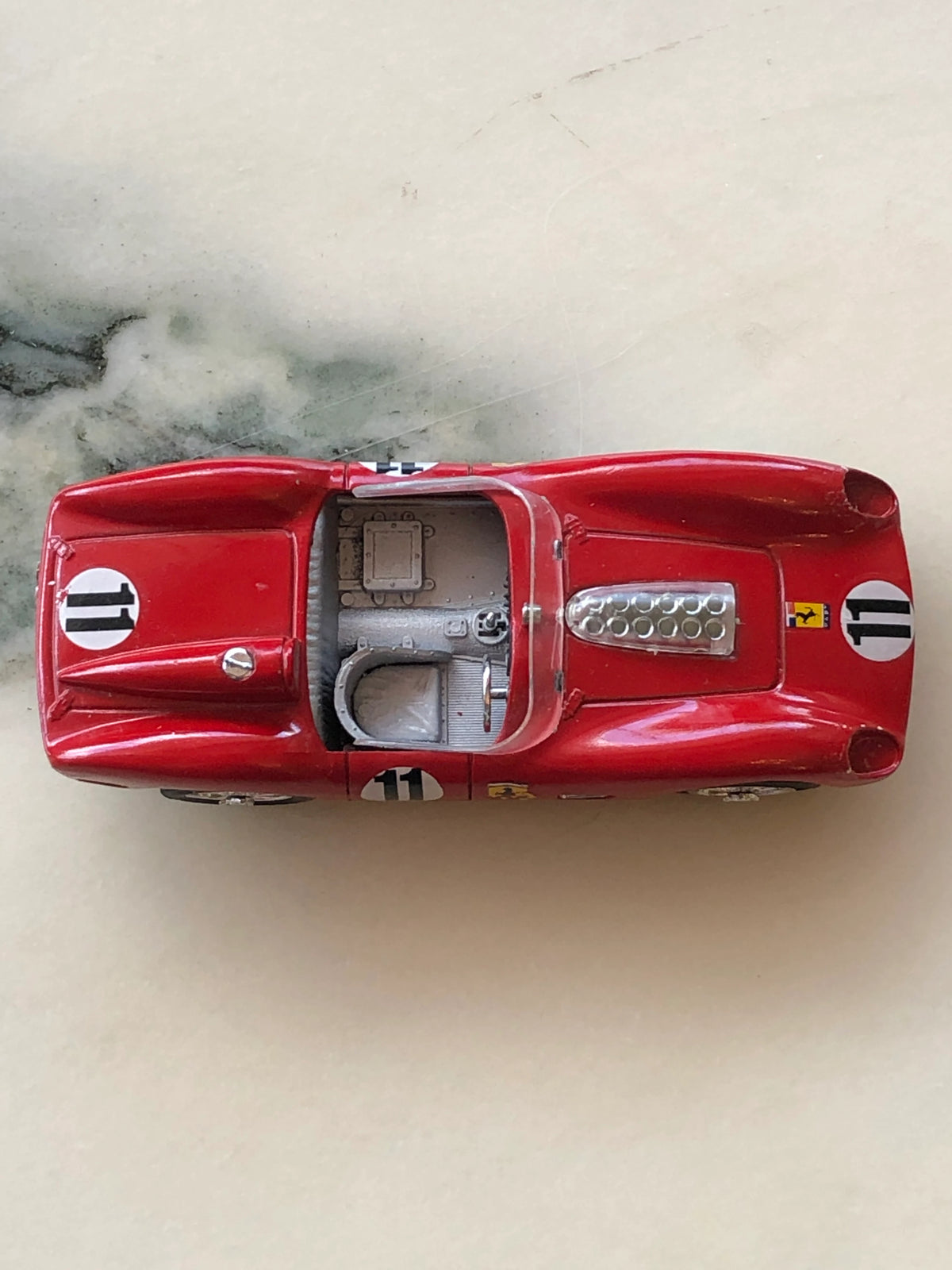 Broochella Rosso Sprint No.11 Vintage Racing Car Brooch photographed from above, featuring a glossy red body, number 11 racing decals, open grey cockpit, clear windscreen and exposed silver engine detailing.