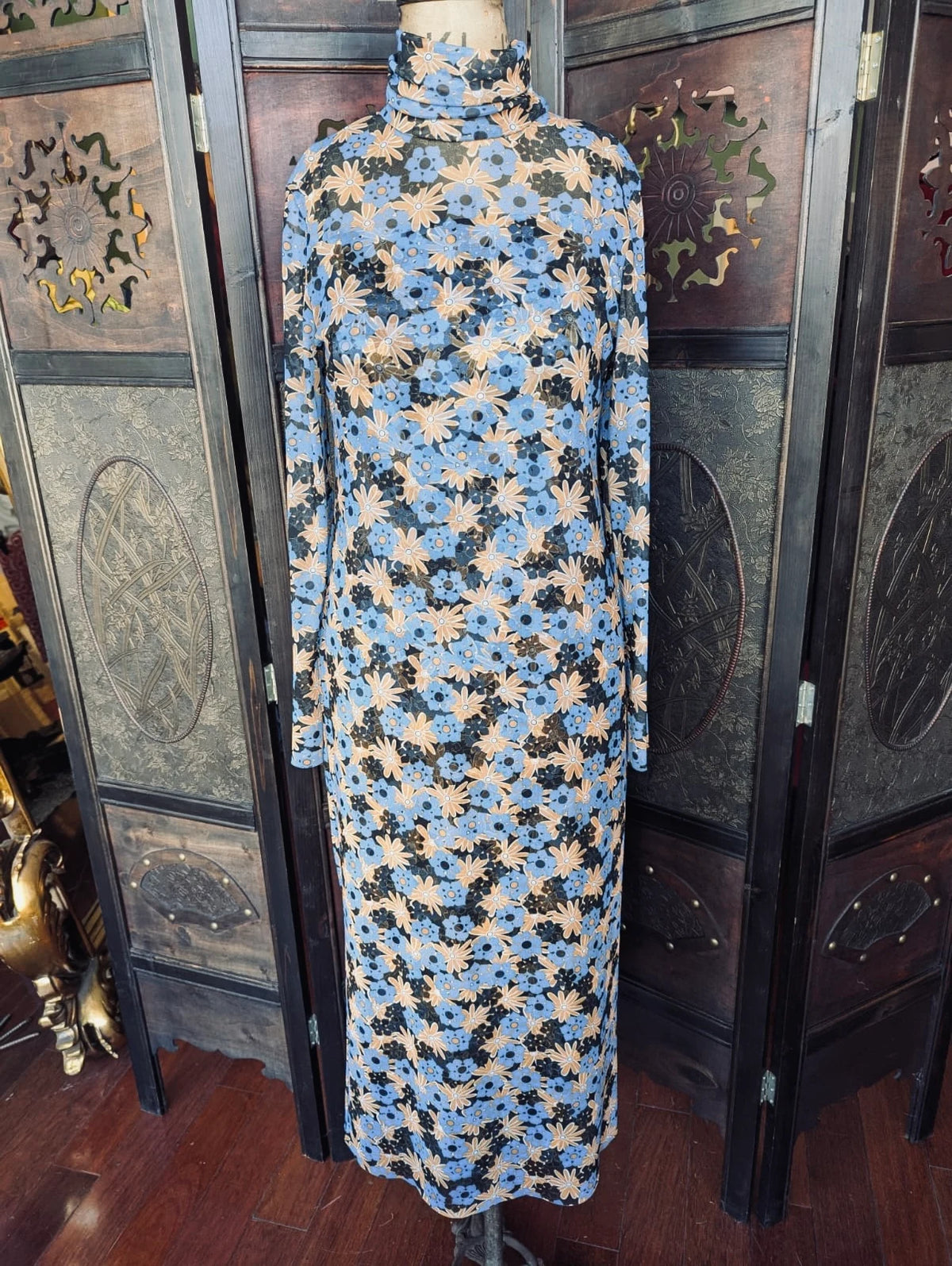 Broochella Scanlan Theodore long sleeve mesh maxi dress in blue orange and black floral print. It is pictured on a vintage mannequin. The background is an ornate dark wood room divider.