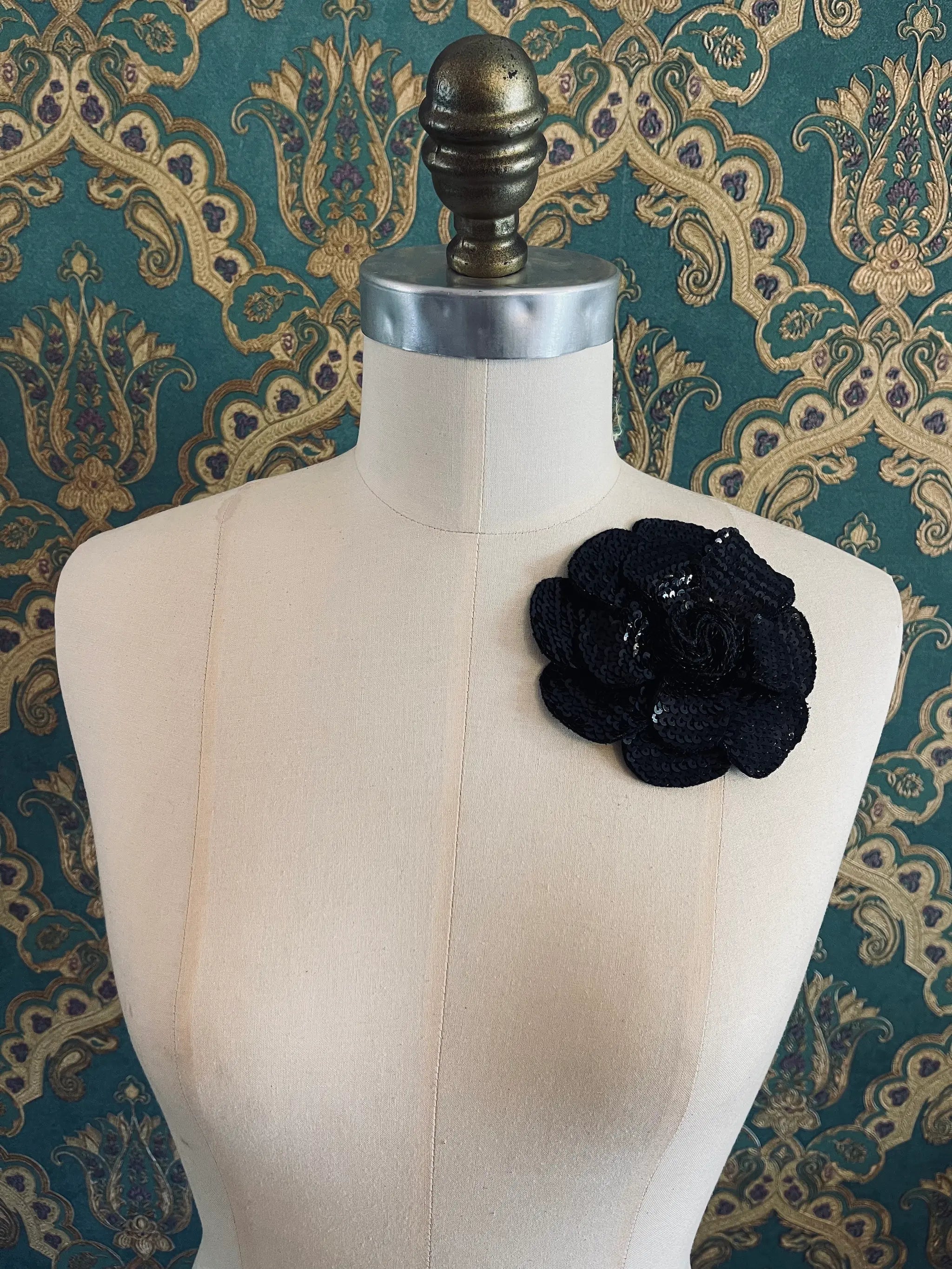 Broochella Scintillante handmade sequin flower brooch on black. Pictured on a mannequin. The background is green and gold damask wallpaper