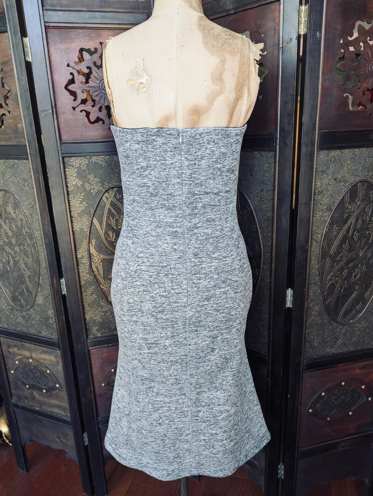 The back view of a Broochella Shakuhachi Strapless Grey Knit Dress – Size S displayed on a dress form mannequin, set against a dark wooden folding screen.