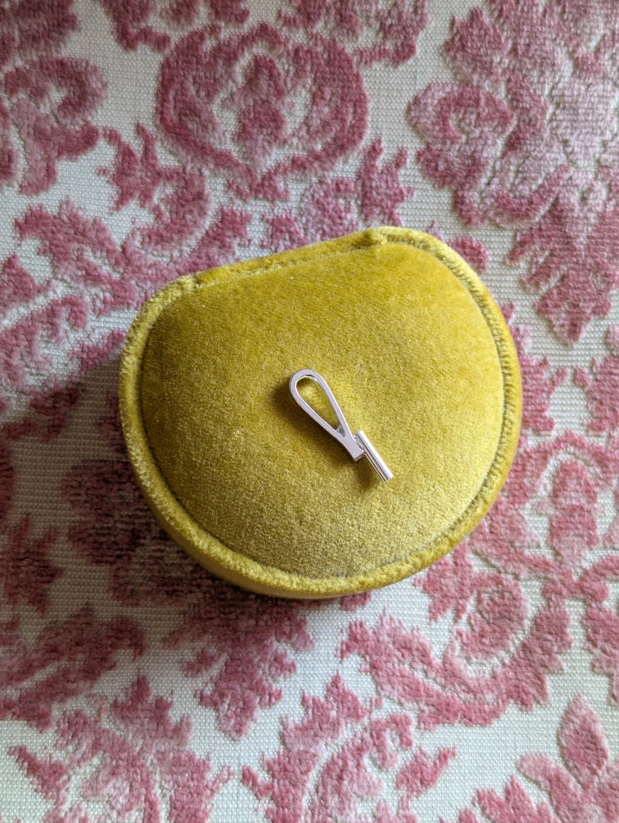 Broochella silver vertical brooch to necklace converter. Pictured on a chartreuse velvet ring box. The background is pink damask fabric.